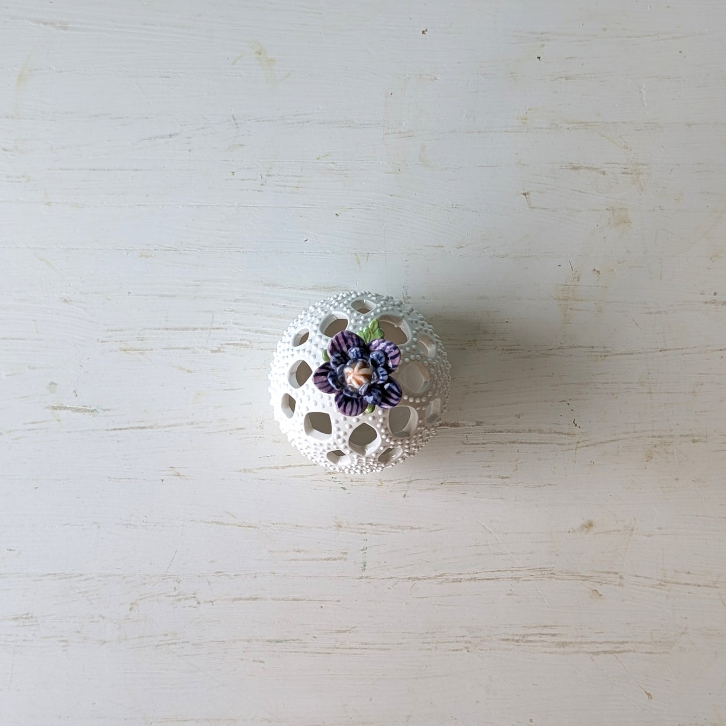 Decorative white ceramic vase with purple flowers on a light wooden surface