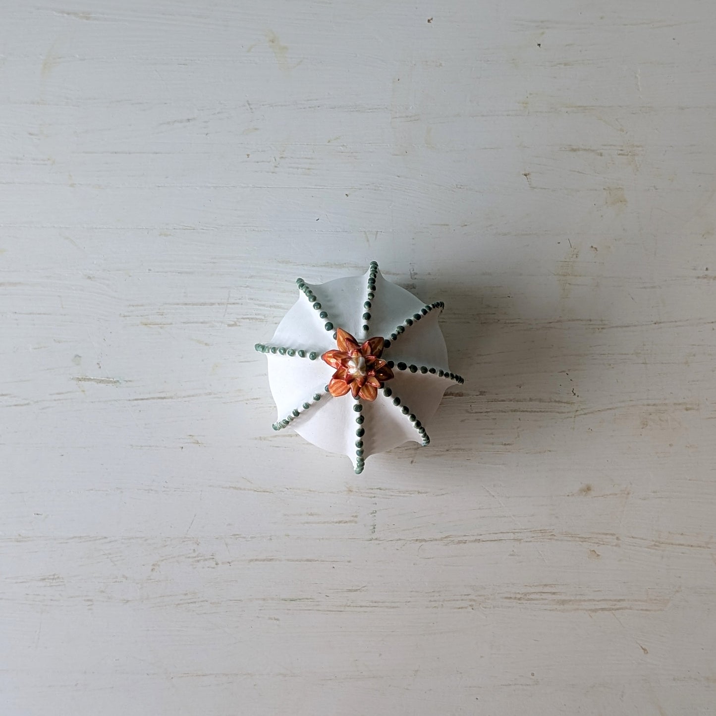 Decorative white vase with green accents and an orange flower accent on a light wooden surface.
