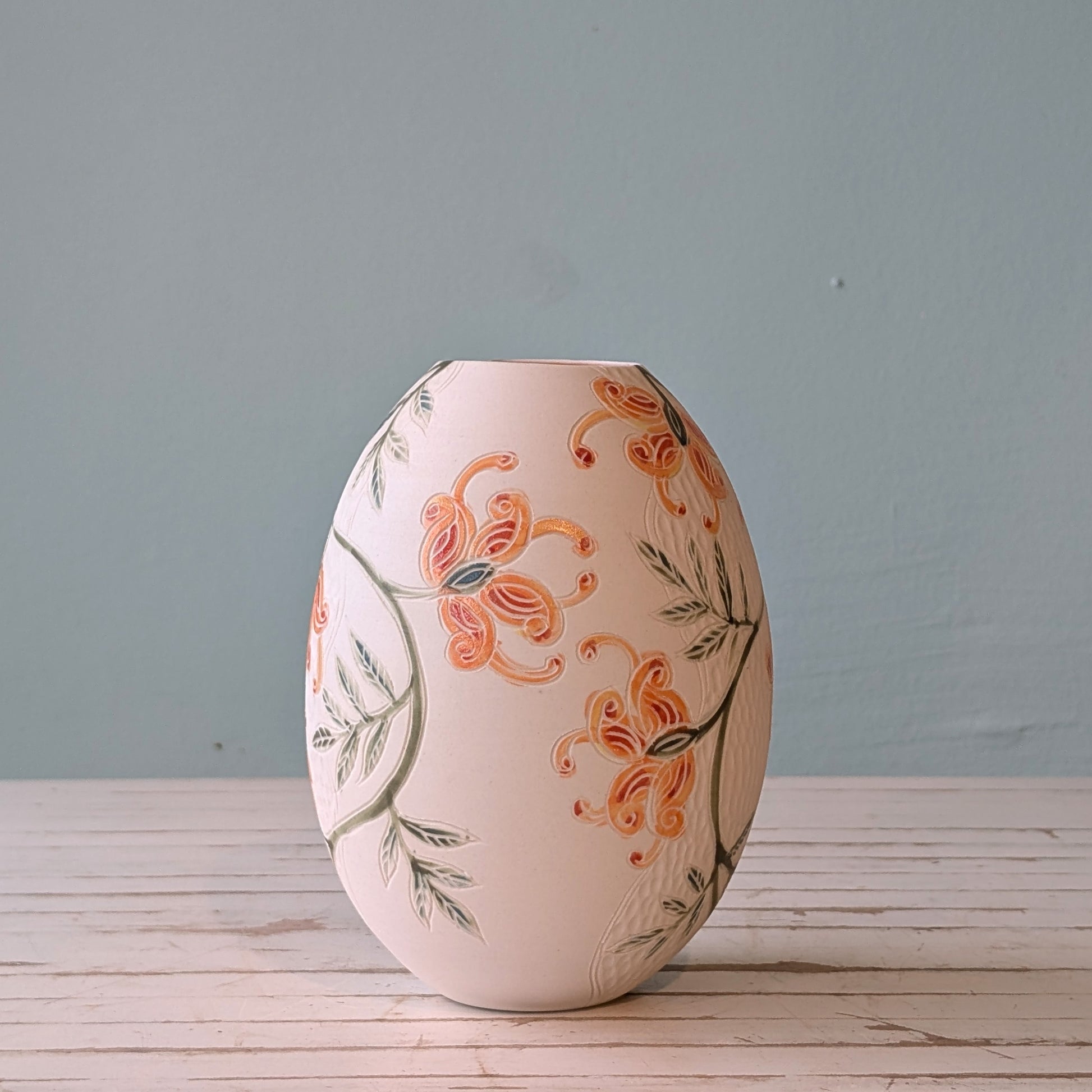 Side view of a white porcelain vase with orange flower pattern and carving