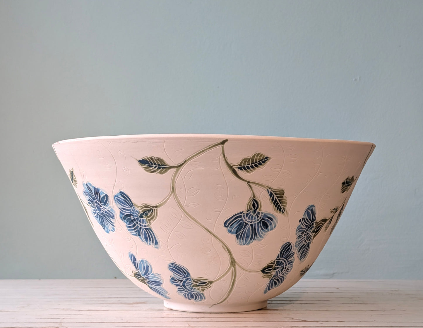 Side view of a large white porcelain bowl with blue flower pattern and carving
