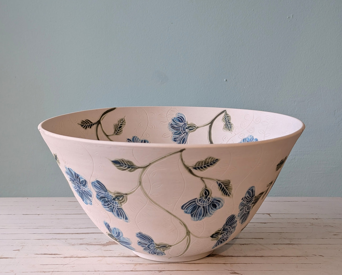 Side view of a large white porcelain bowl with blue flower pattern and carving