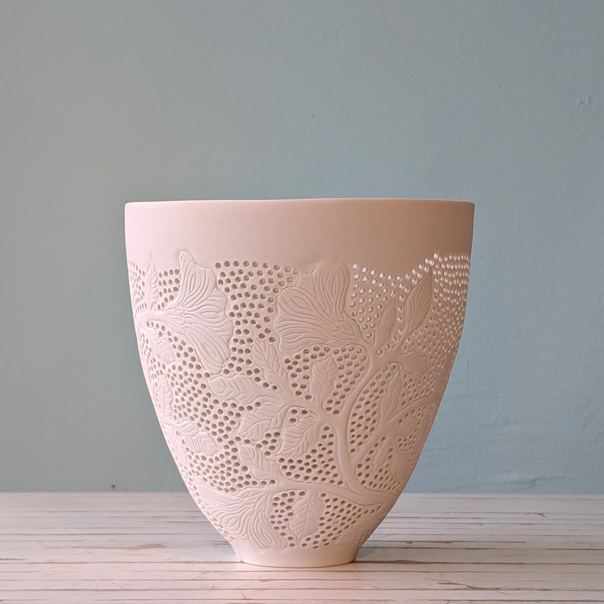 Side view of a large white porcelain bowl with carving and cut outs.