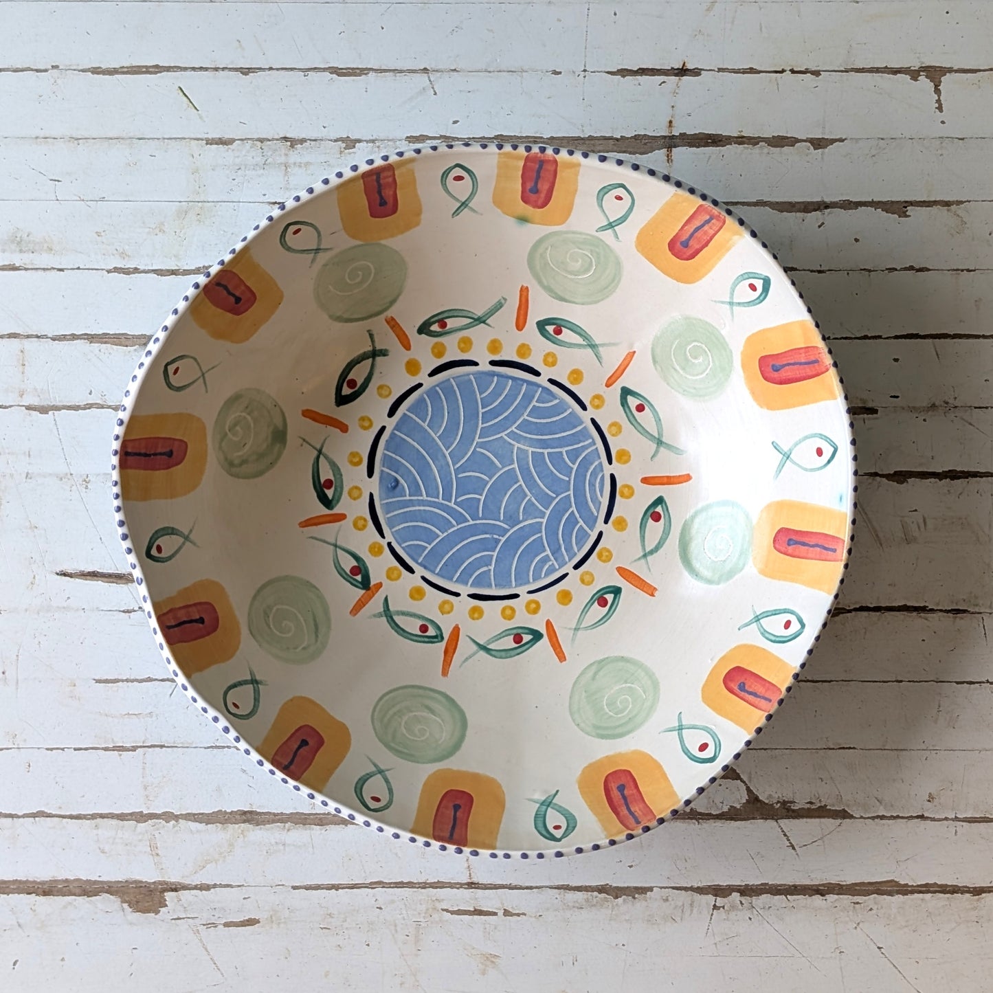 Top view of a colourful ceramic bow with fish design on a white wooden surface.