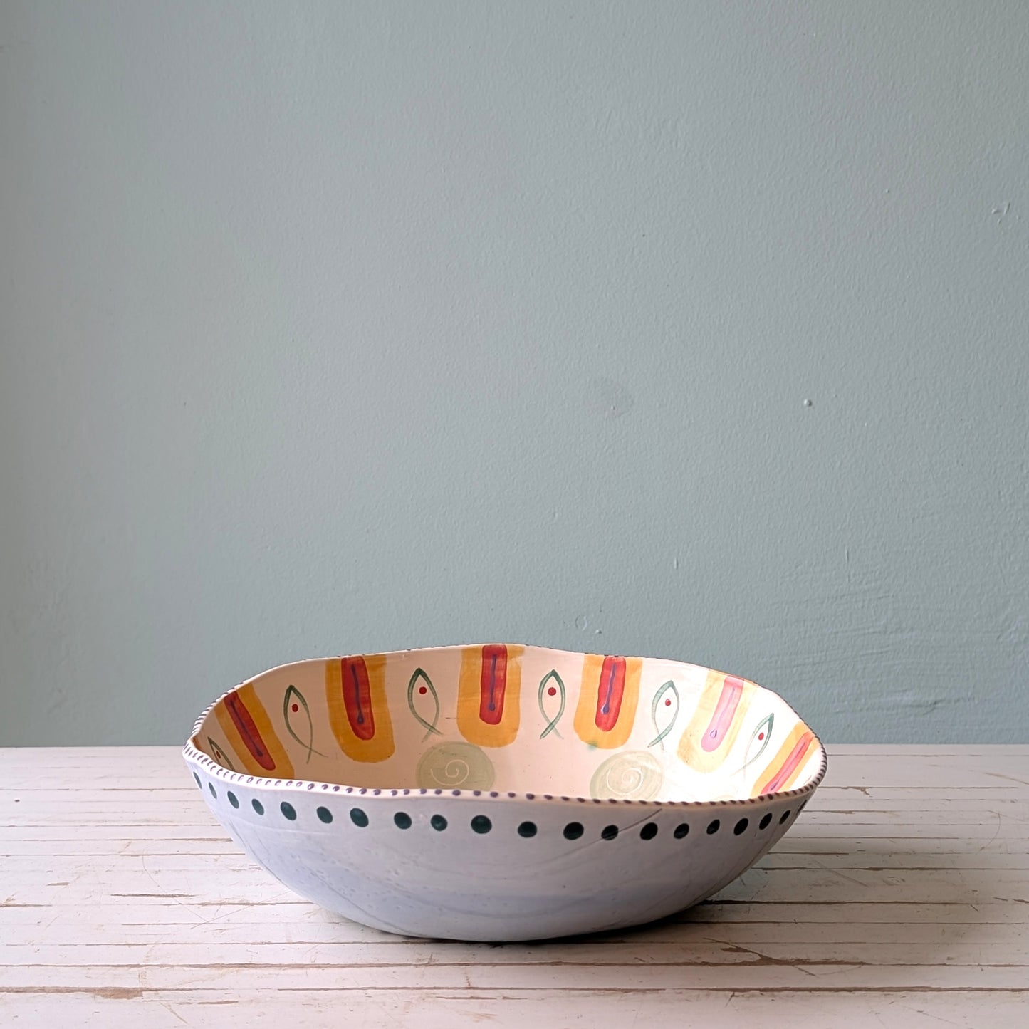 Decorative ceramic bowl with fish pattern on a wooden surface and blue wall background