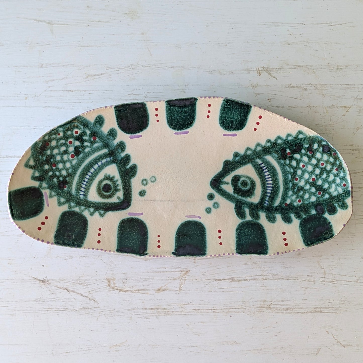 Beige ceramic platter with green fish design on white table