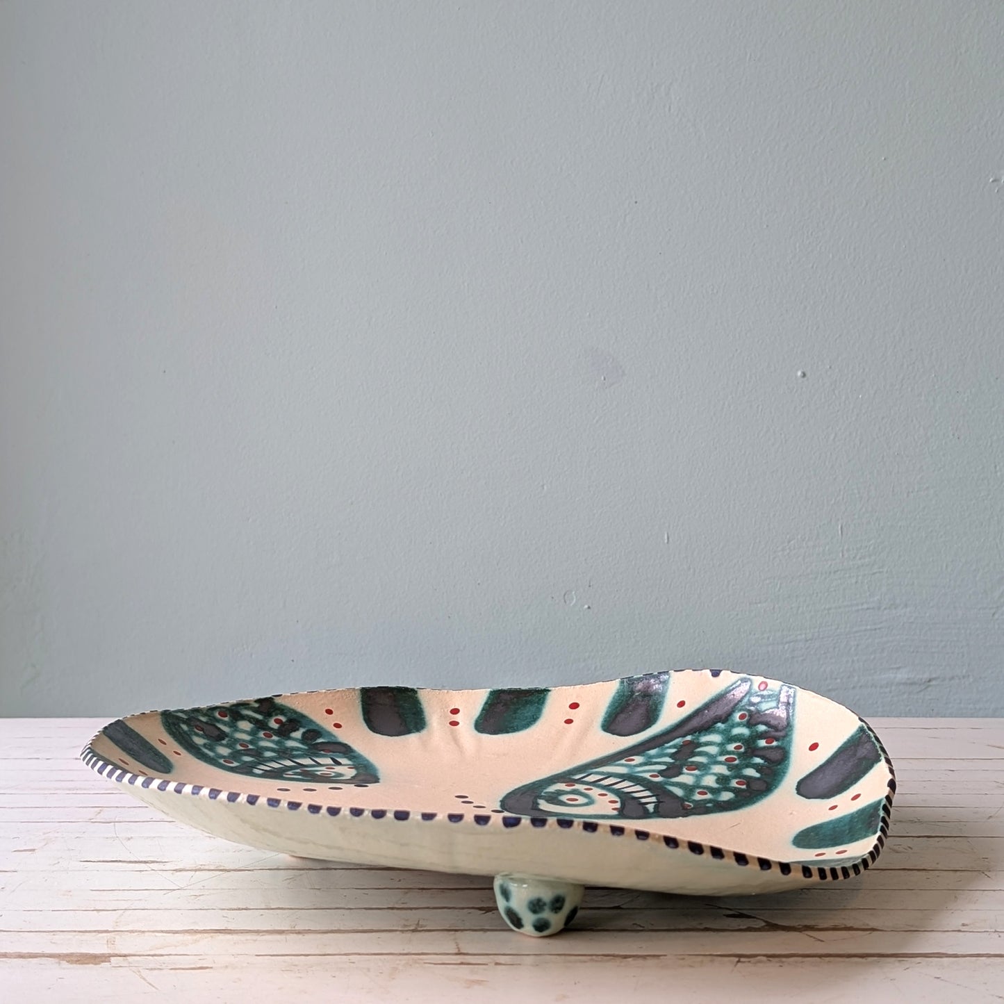 Front view of a white ceramic serving platter with green fish design on a white wooden table with blue background.