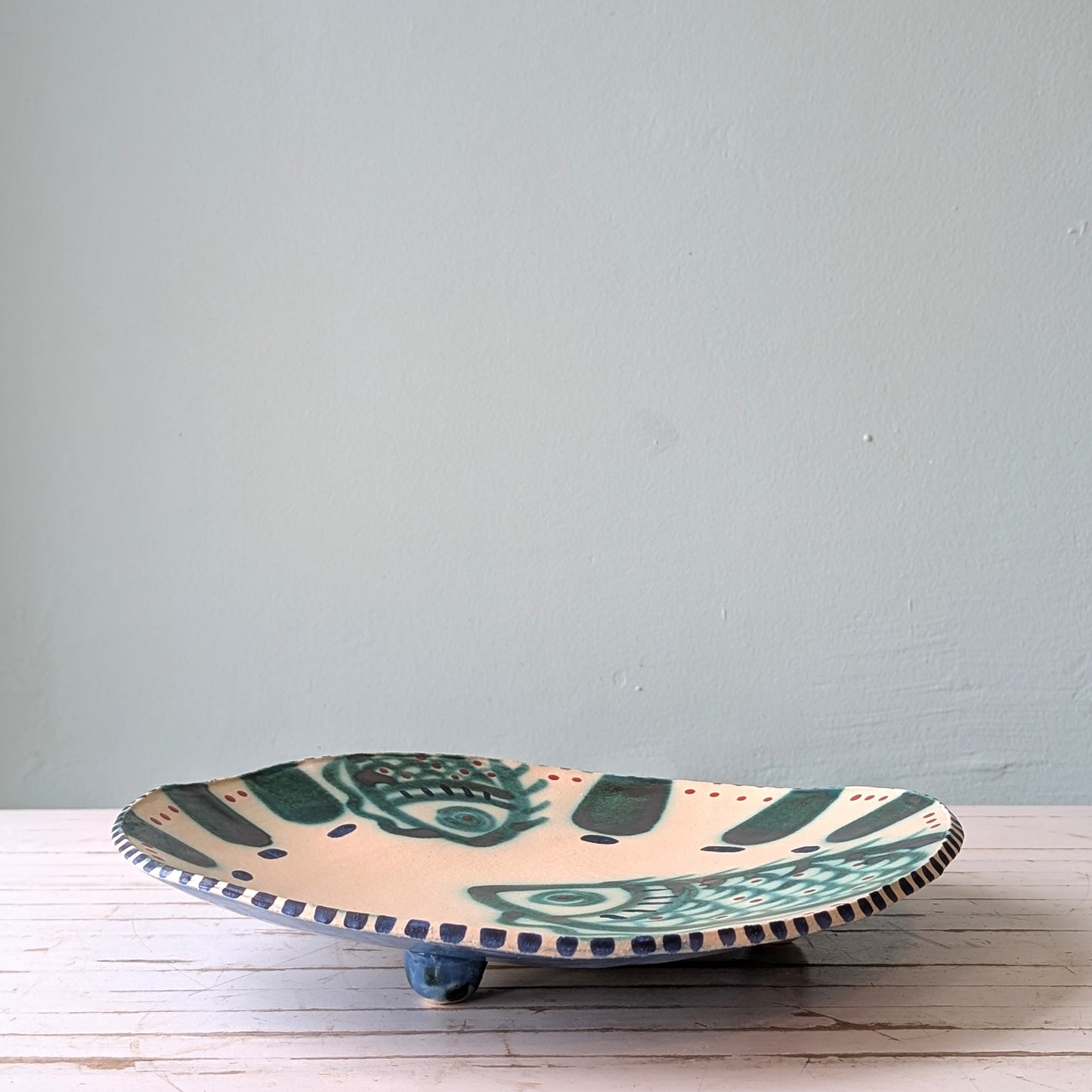 Ceramic plate with decorative design on a light wooden surface against a plain wall.