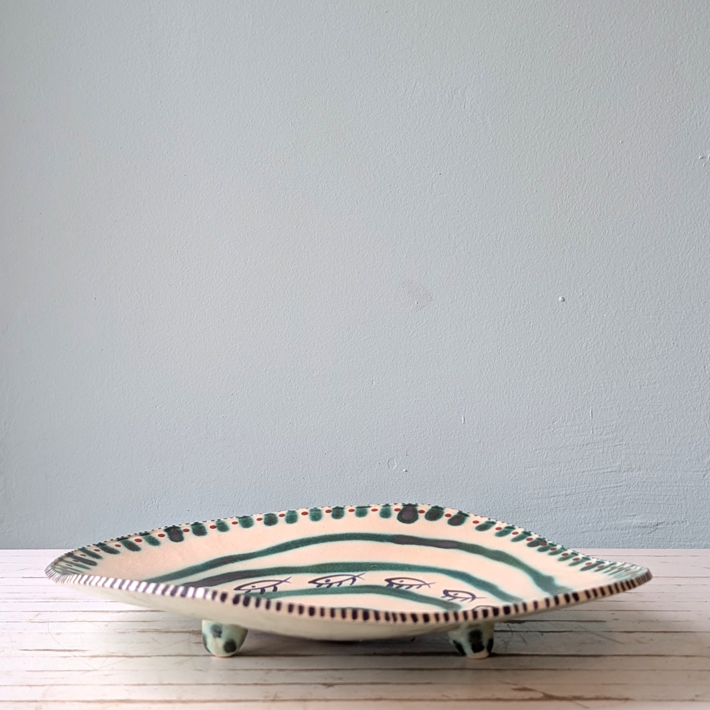 Ceramic plate with green and blue patterns on a wooden surface against a gray wall.