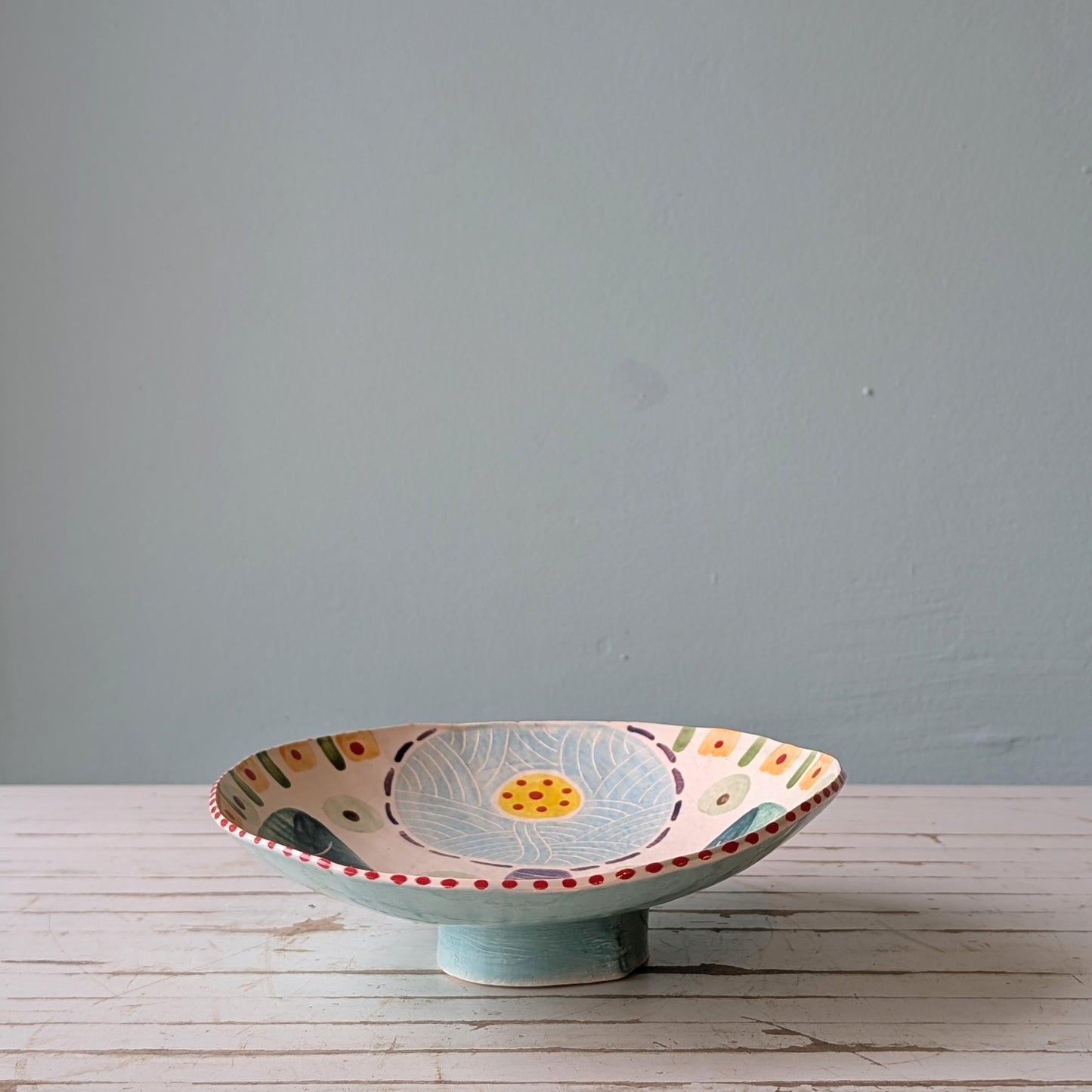 Decorative ceramic bowl with floral design on a wooden surface against a gray wall