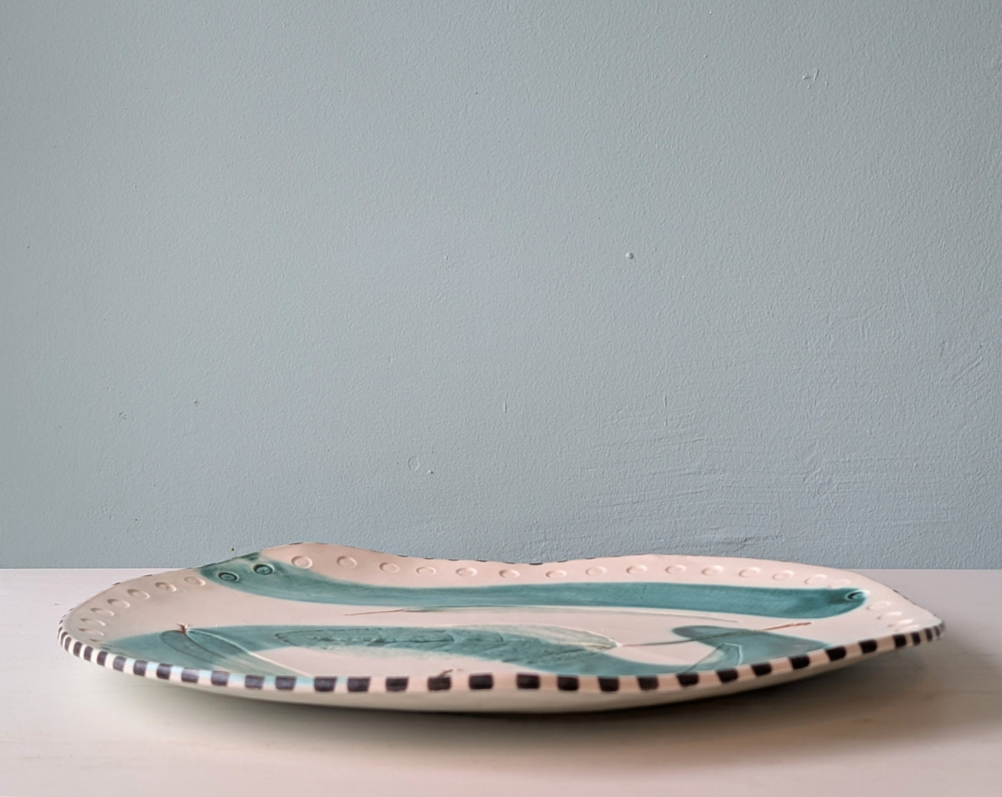 Ceramic platter with green leaf pattern on a white table against a blue wall