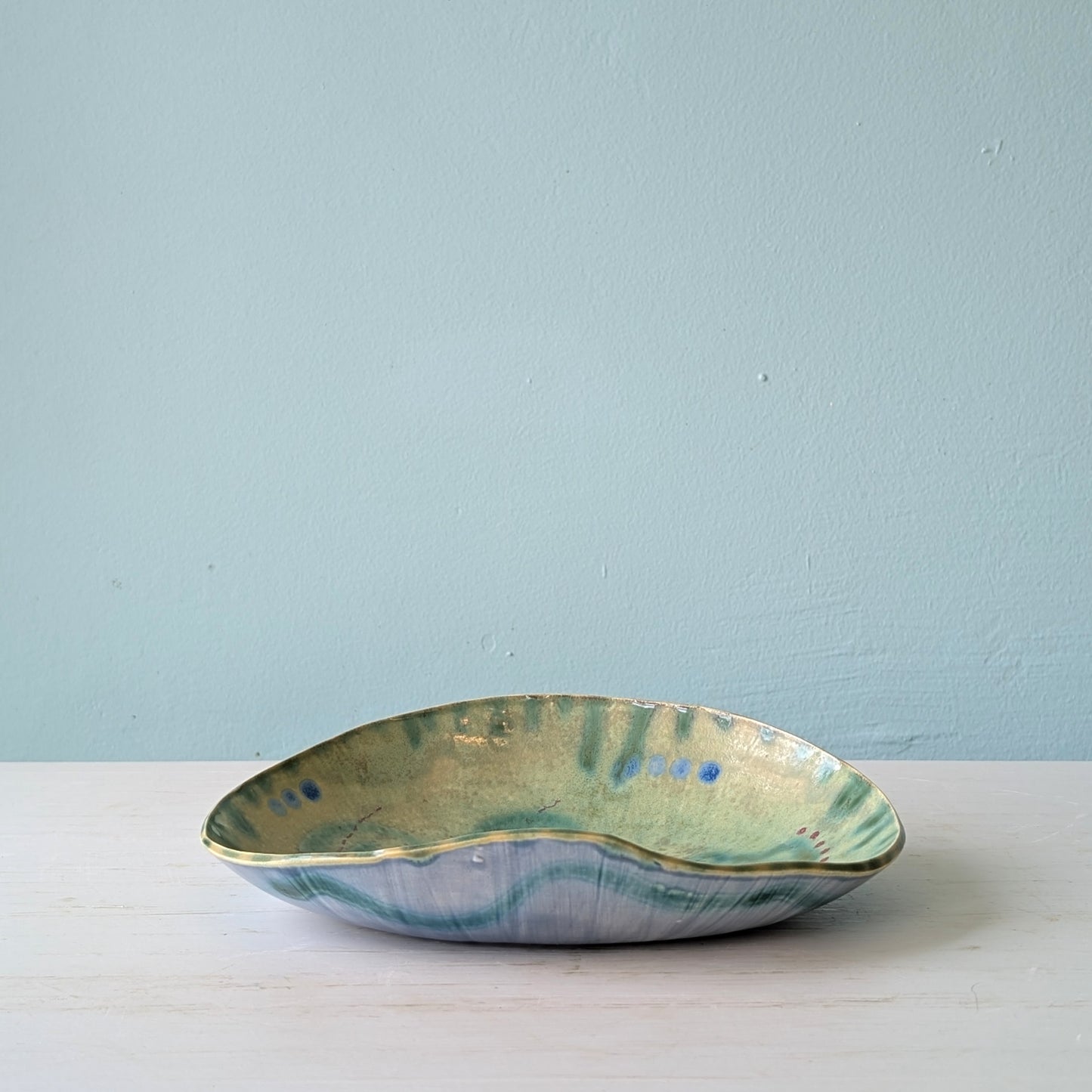 Ceramic bowl with green and blue glaze on a light blue background