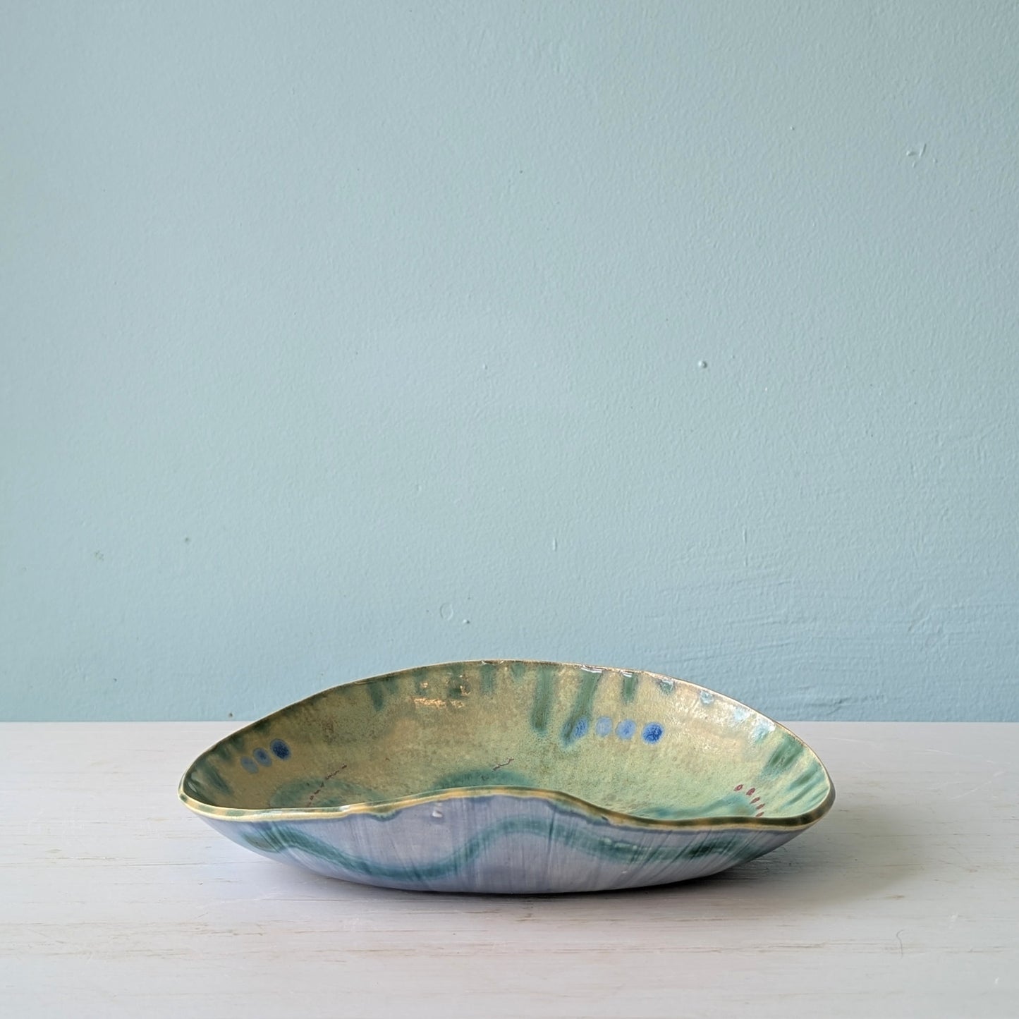 Ceramic bowl with green and blue glaze on a light blue background