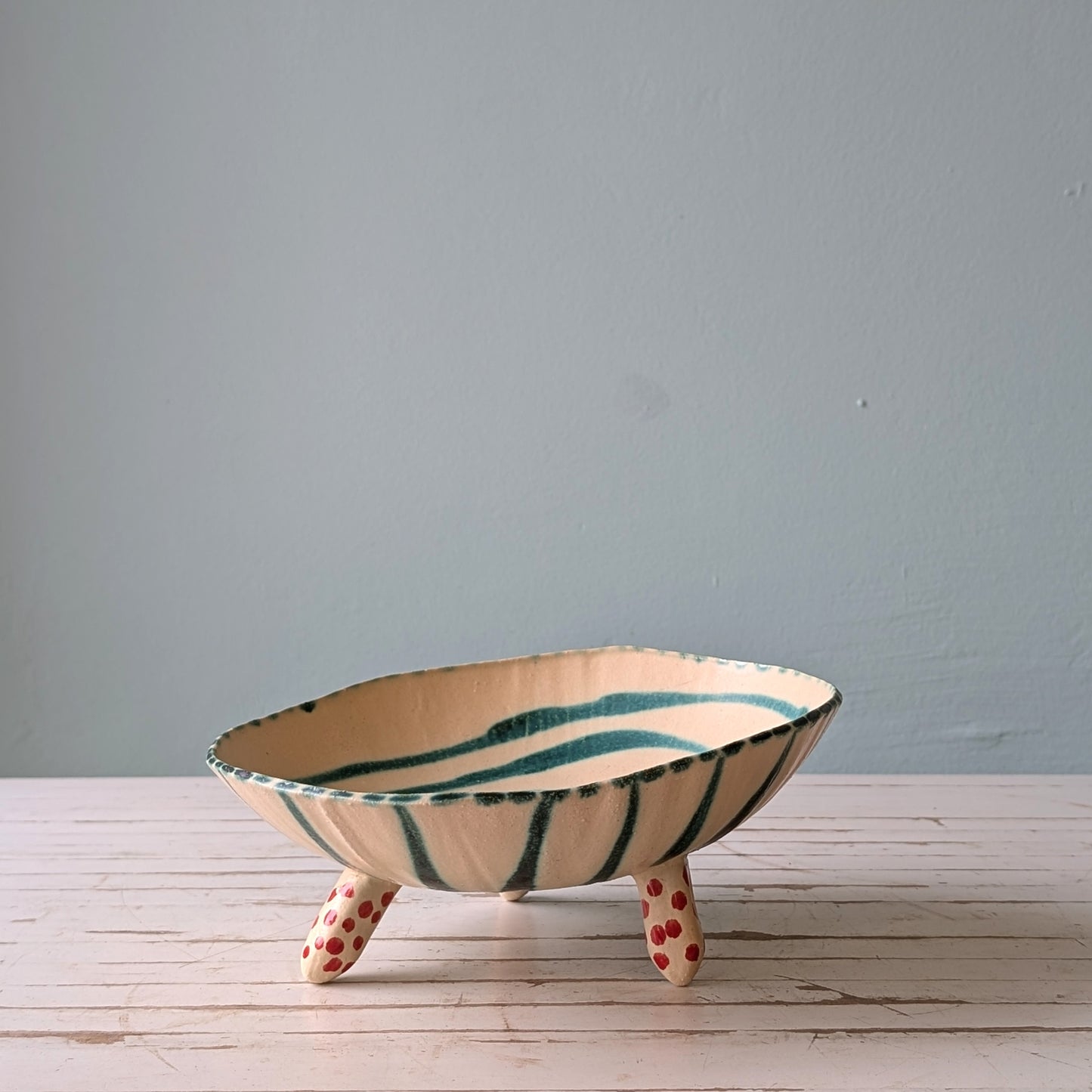 Front view of a white footed ceramic bowl with green stripes on a white wooden table.