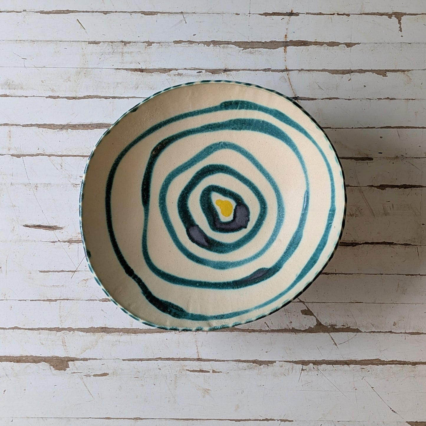 White ceramic bowl with green concentric circle design on a wooden surface
