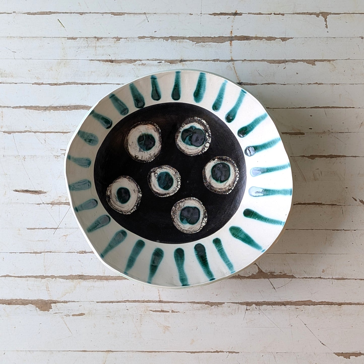 Top view of a white ceramic bowl with green abstract pattern on a white wooden surface.
