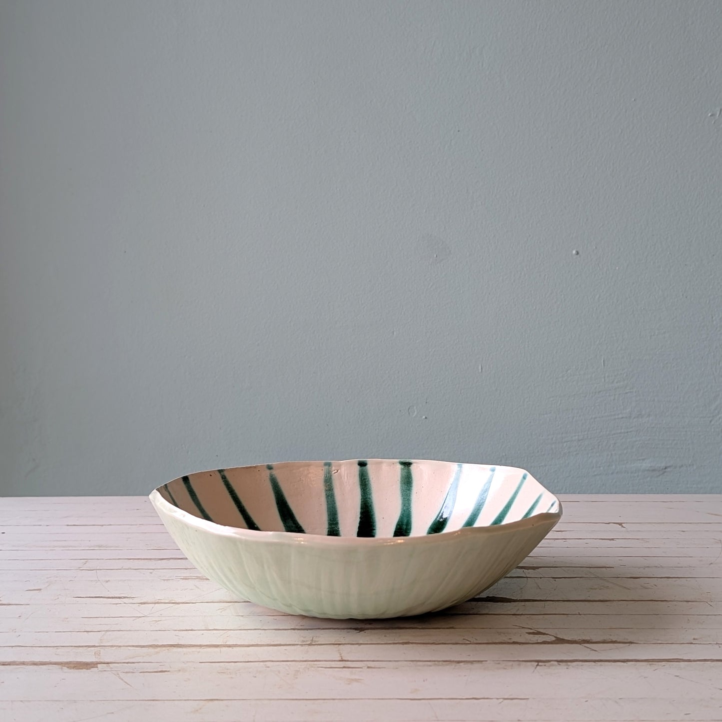 Front view of a white ceramic bowl with green abstract pattern on a white wooden table with blue background.