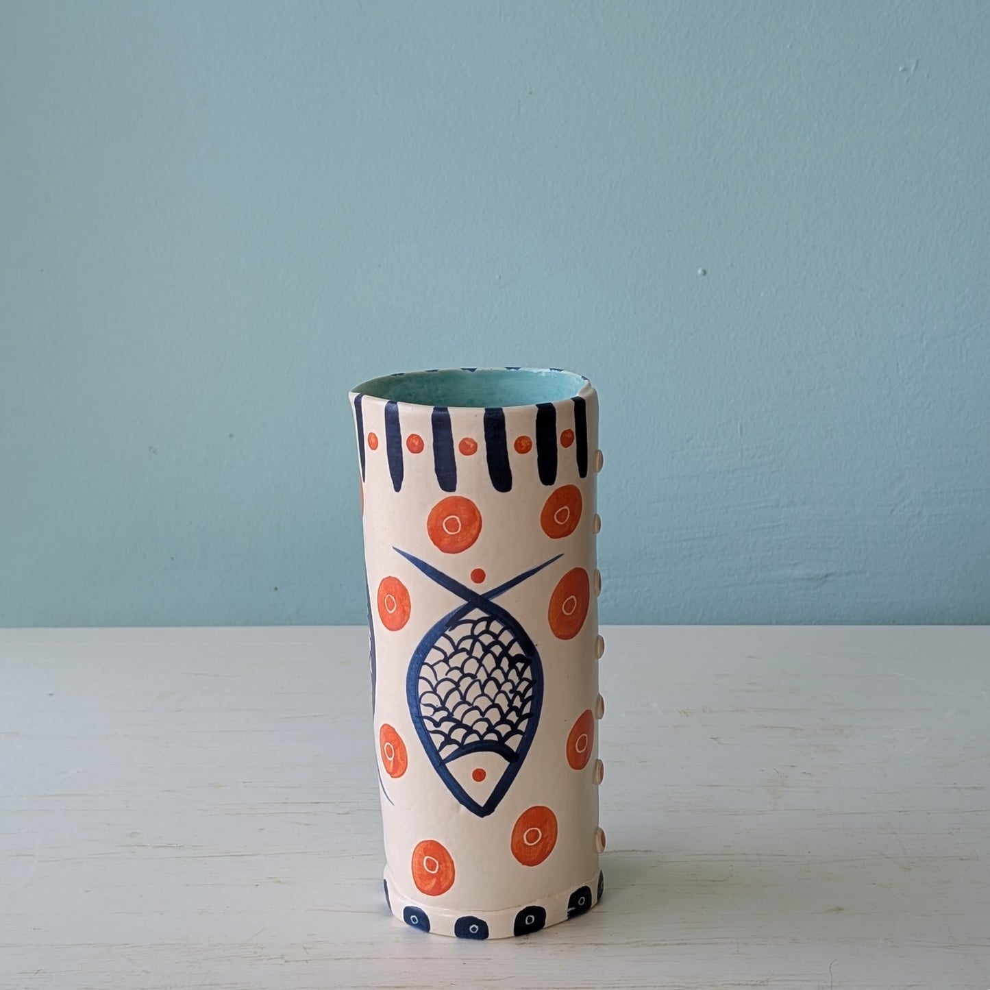 Cylindrical ceramic vase with decorative patterns on a light blue background