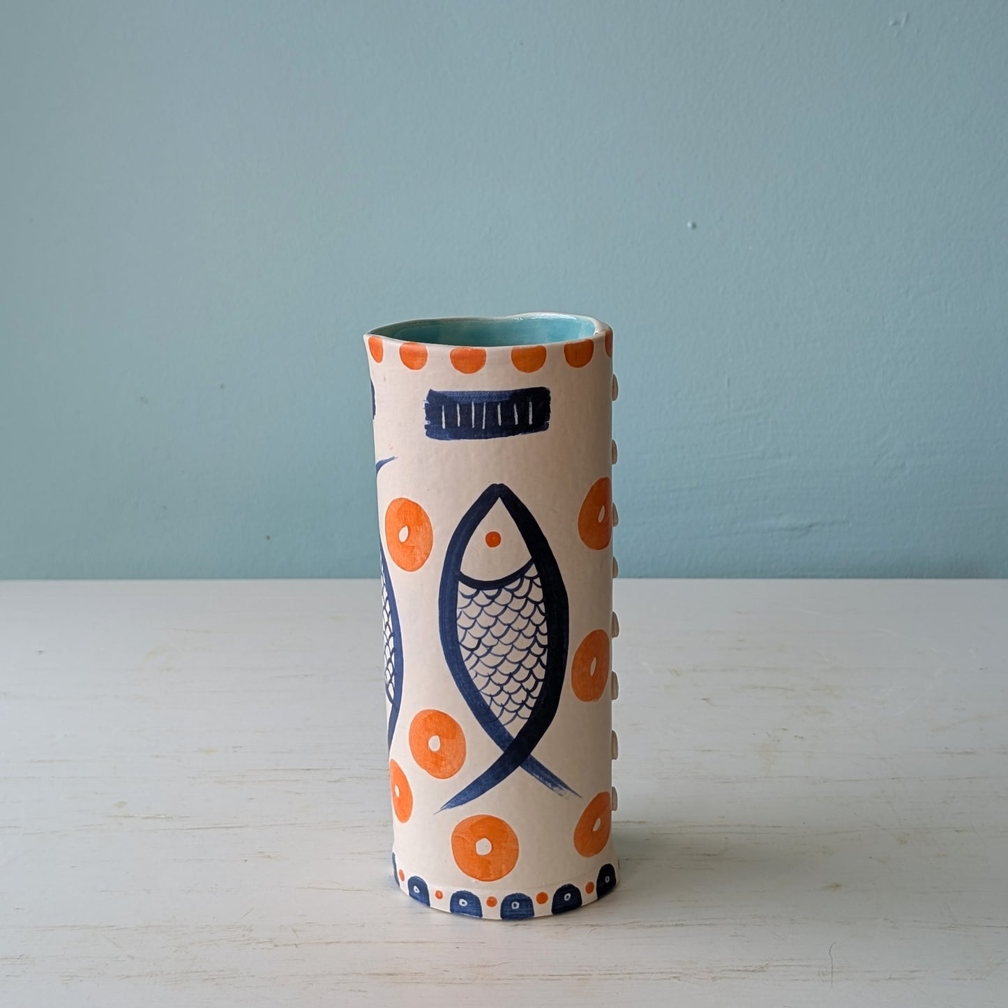 Cylindrical ceramic vase with fish and circle pattern on a light blue background