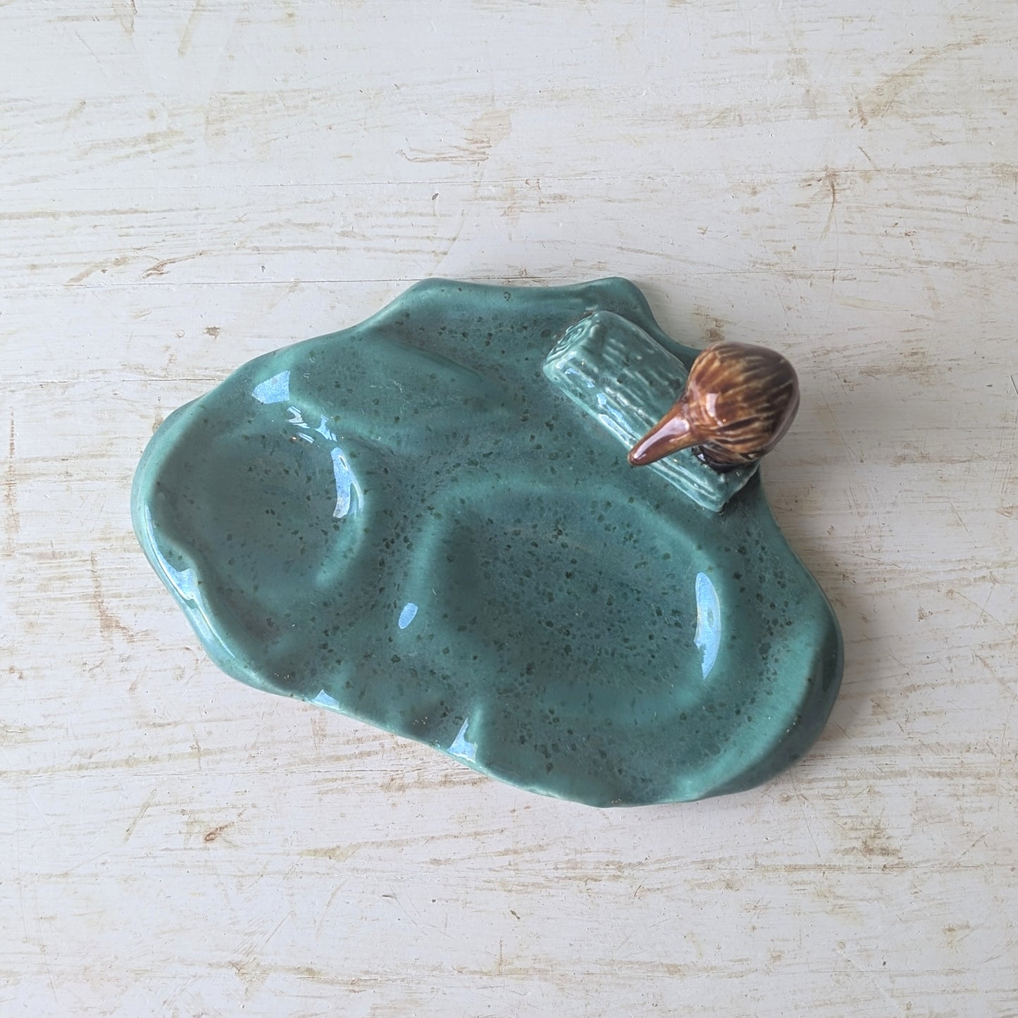 Teal ceramic dish with a small brown kookaburra figurine on a light wooden surface