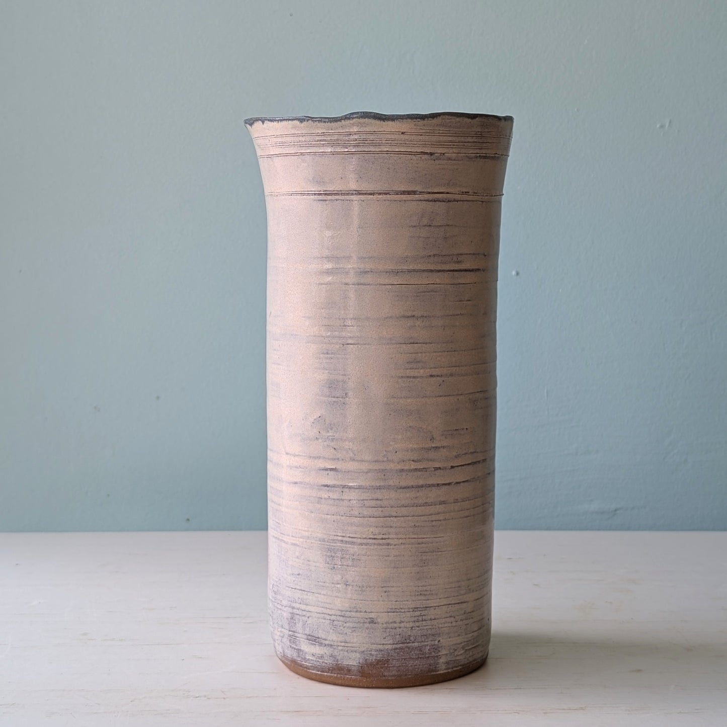 Cylindrical ceramic vase with textured surface on a light blue background