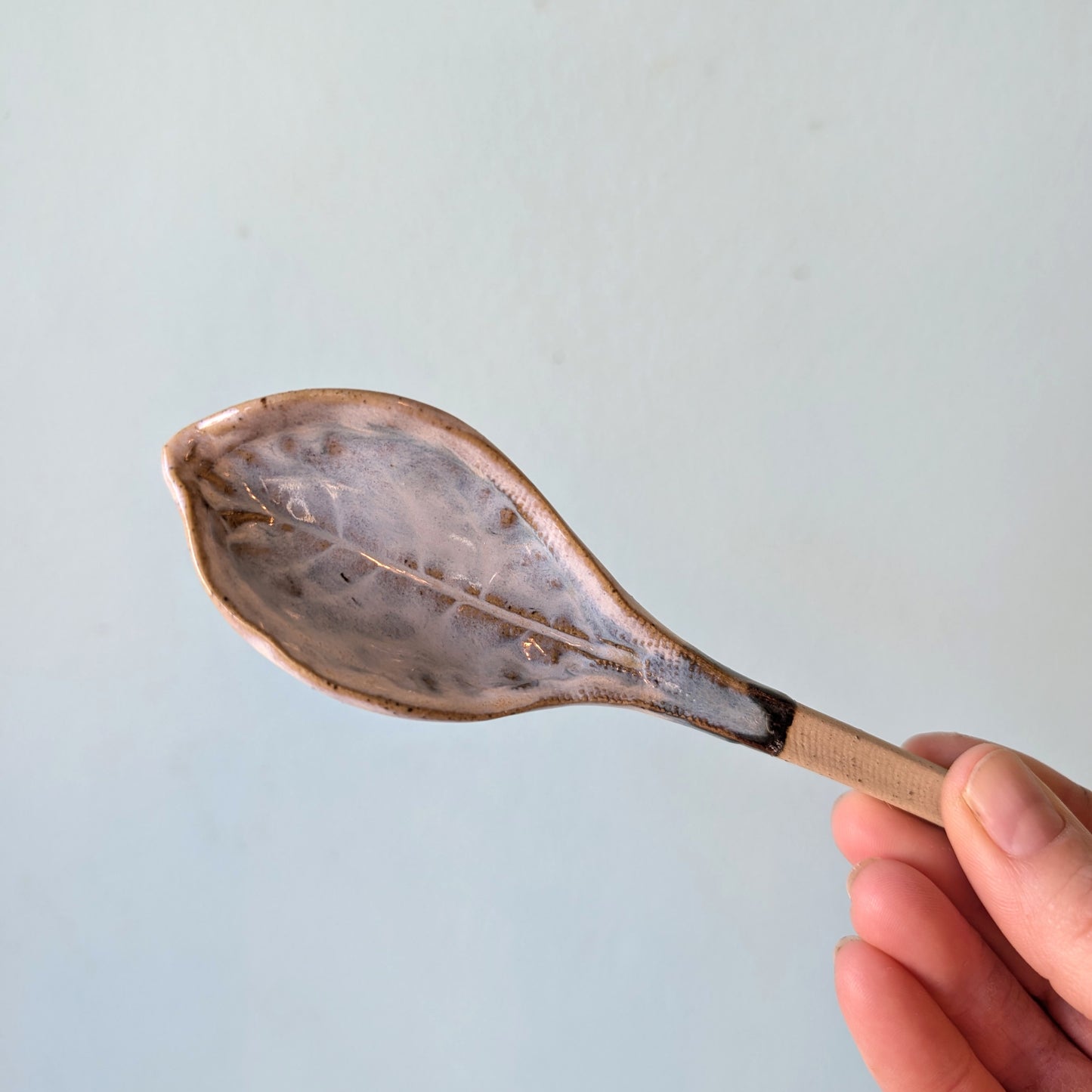 Hand holding a ceramic spoon against a light blue background