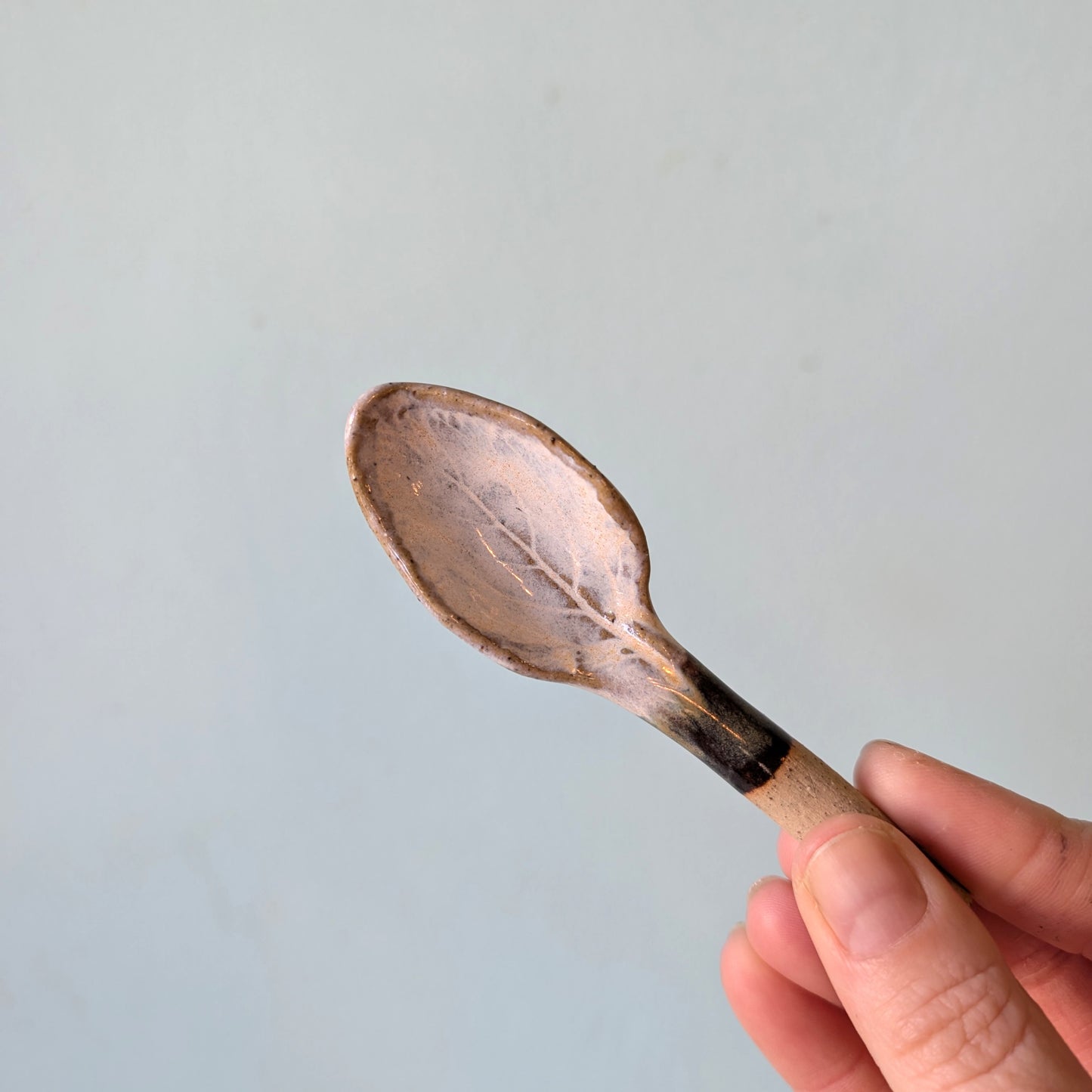 Hand holding a small ceramic spoon against a light blue background