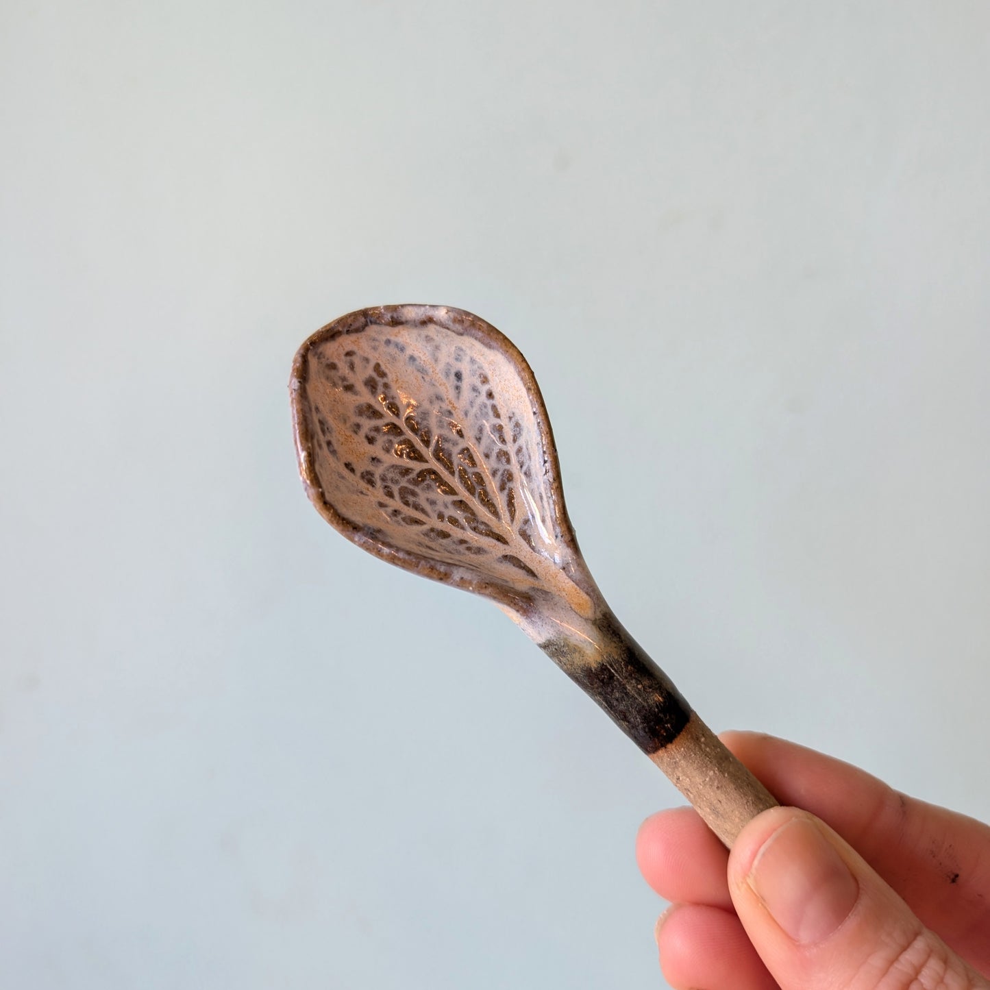 Hand holding a decorative ceramic spoon against a light blue background