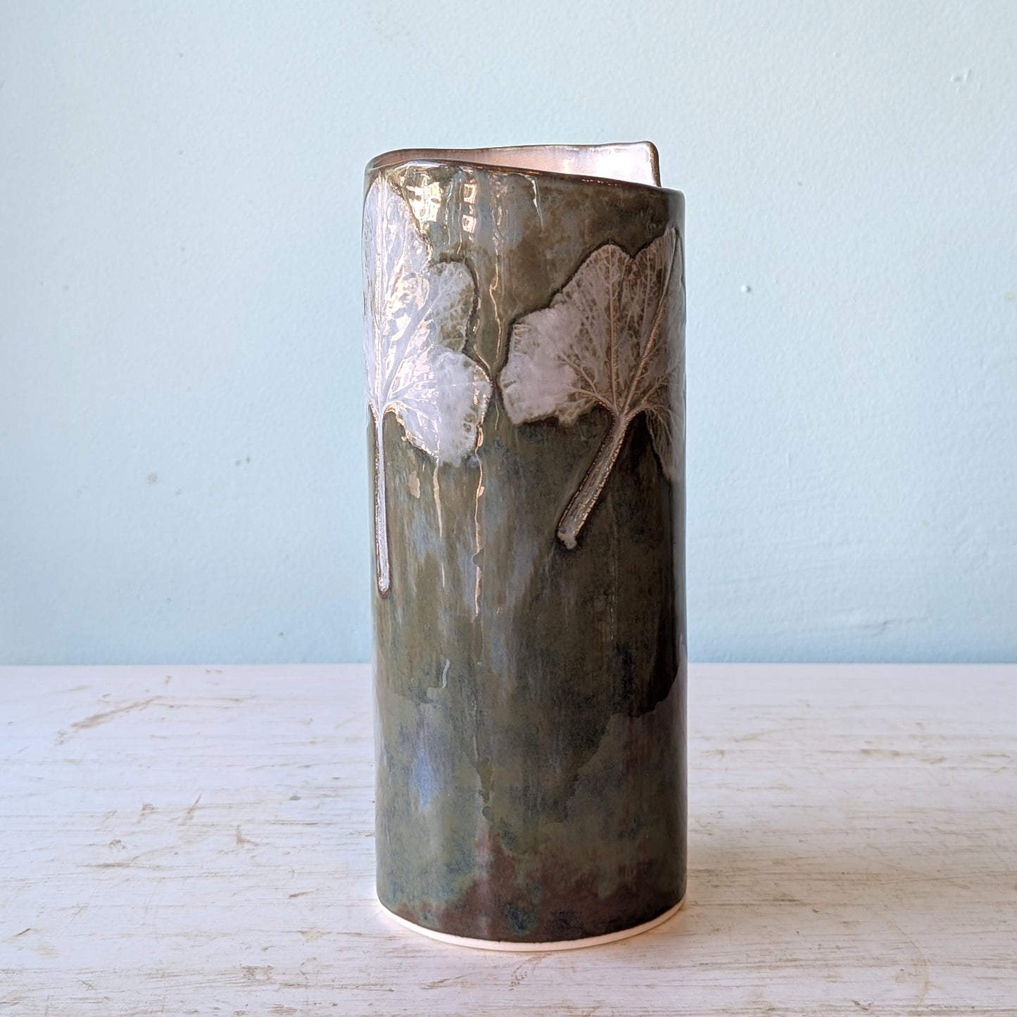 Cylindrical ceramic vase with leaf patterns on a light blue background