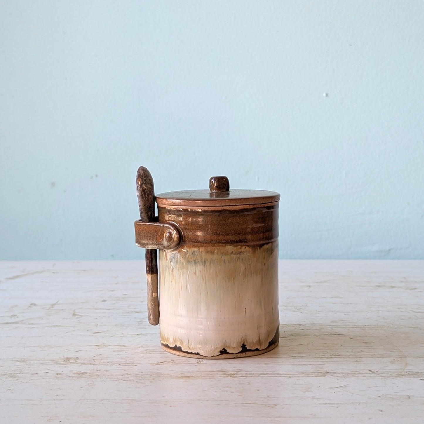Ceramic jar with ceramic handle and spoon on a light blue background