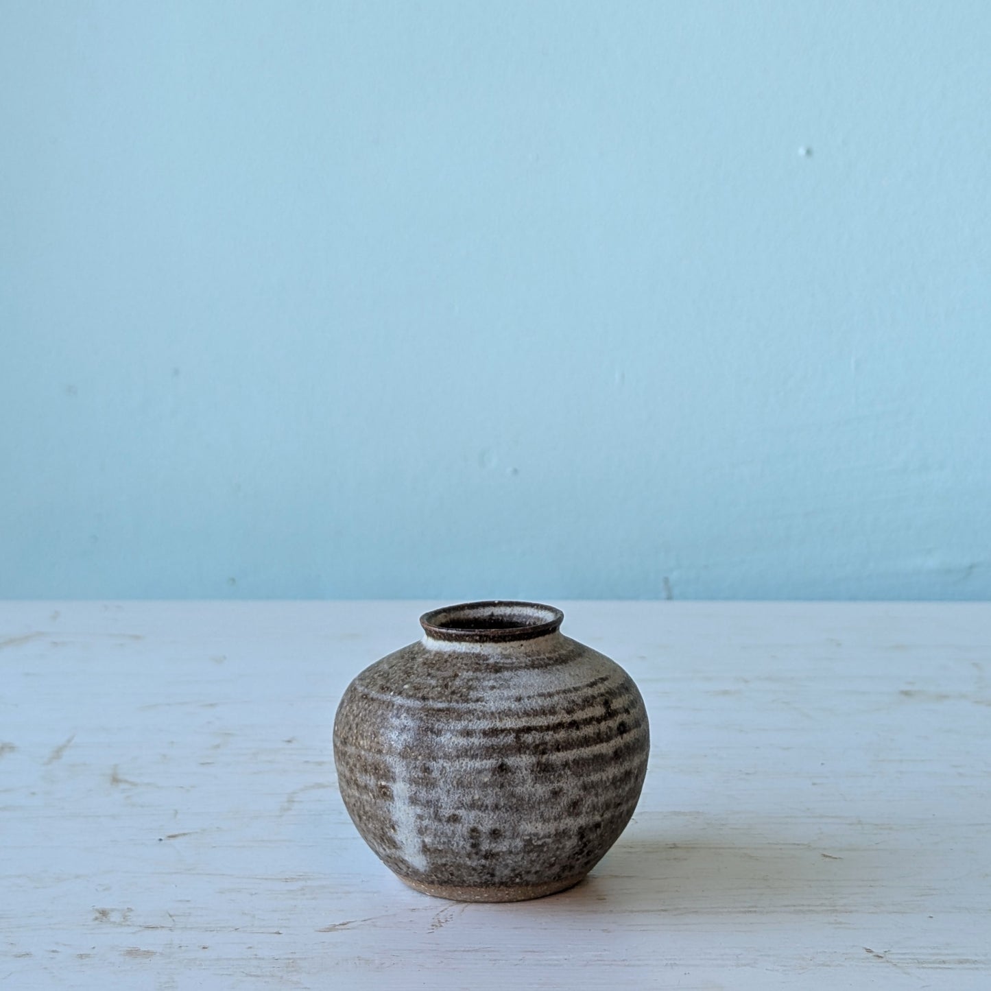 Small ceramic vase on a light wooden surface with a light blue background