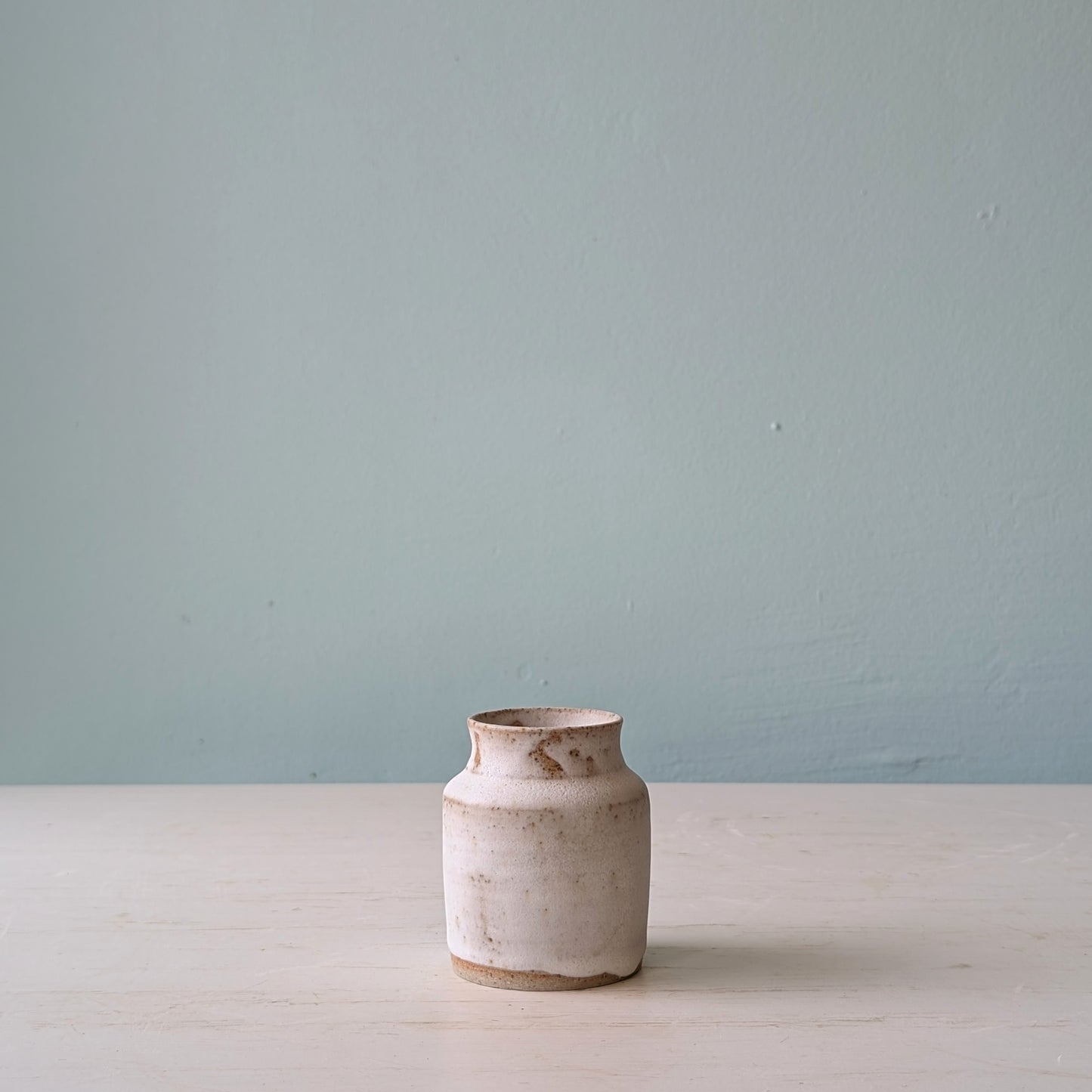 Small white vase on white table against a blue wall