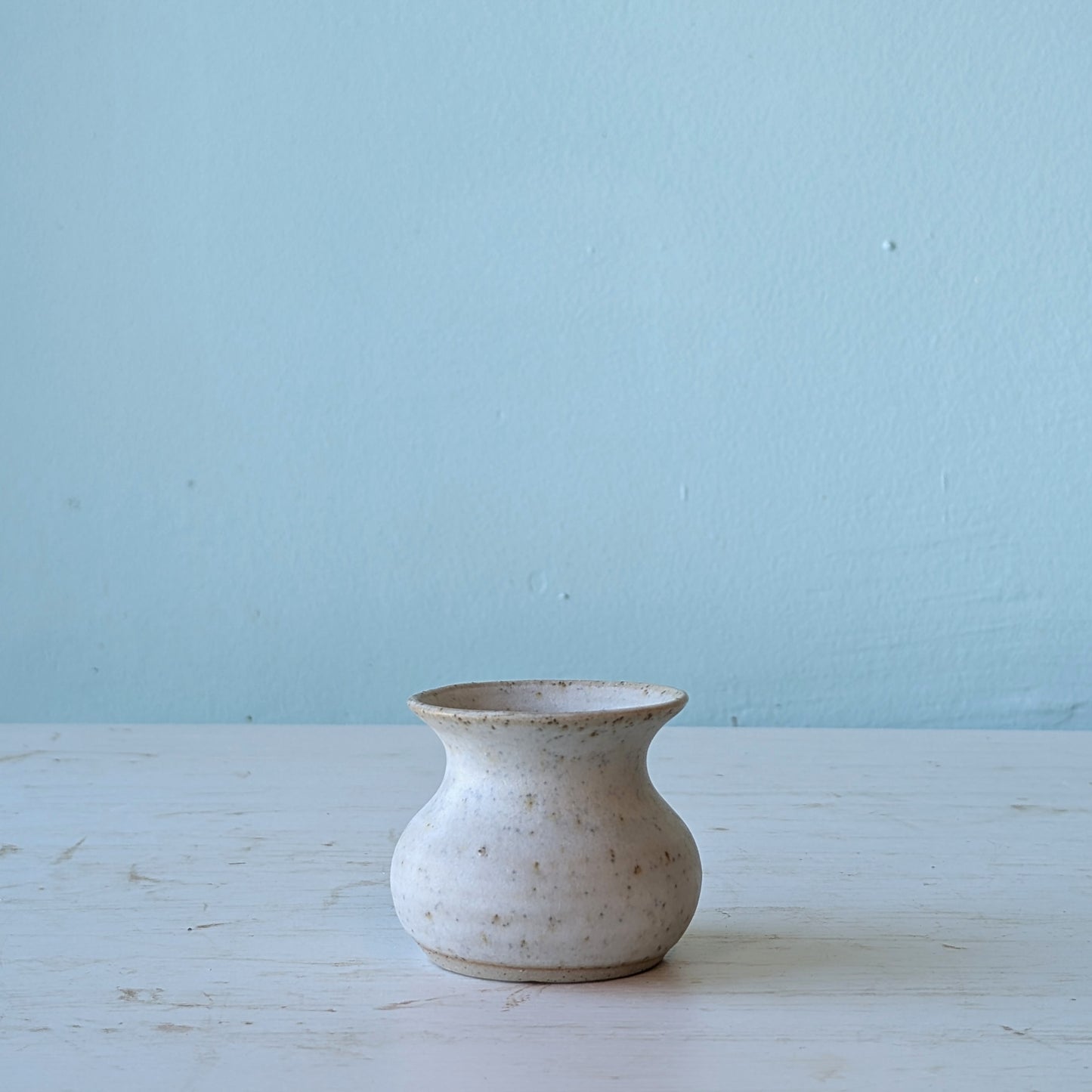 Small ceramic vase on a light blue surface with a light blue background