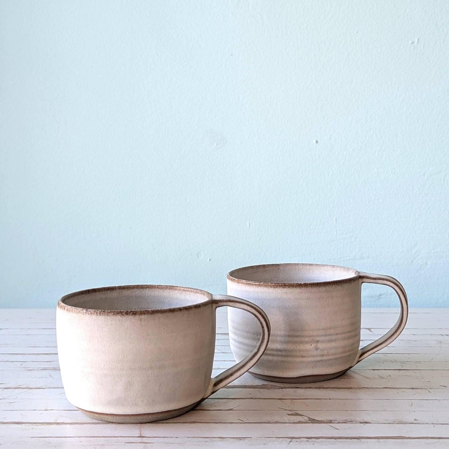 Front view of two ceramic mugs with white slip exterior