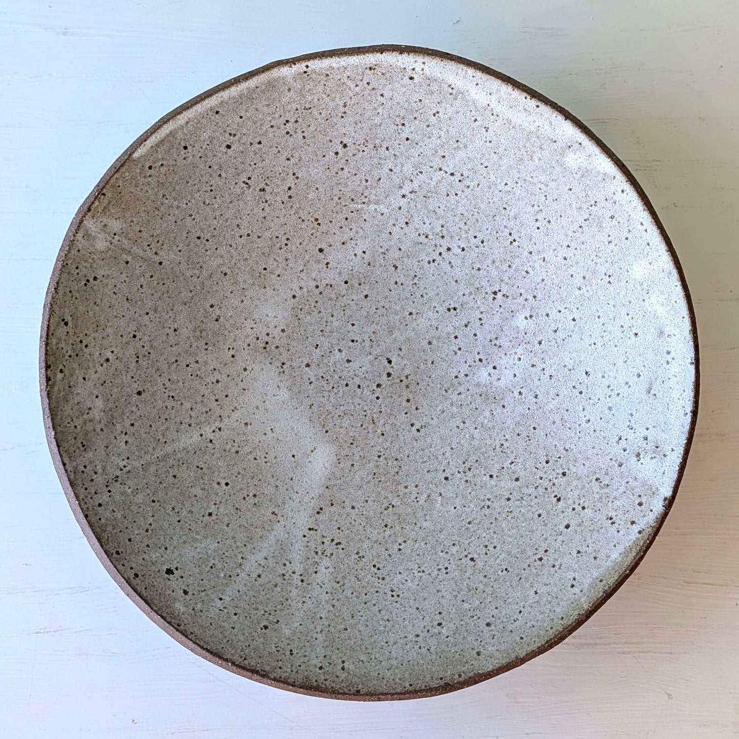 Round ceramic bowl with a speckled texture on a light blue background