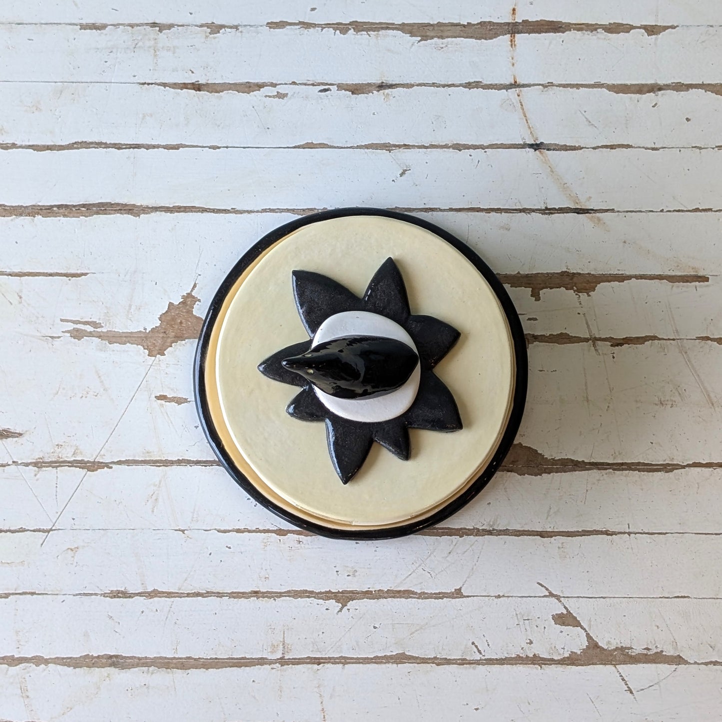 Top view of a butter dish with bird handle in black and white design on a distressed white surface