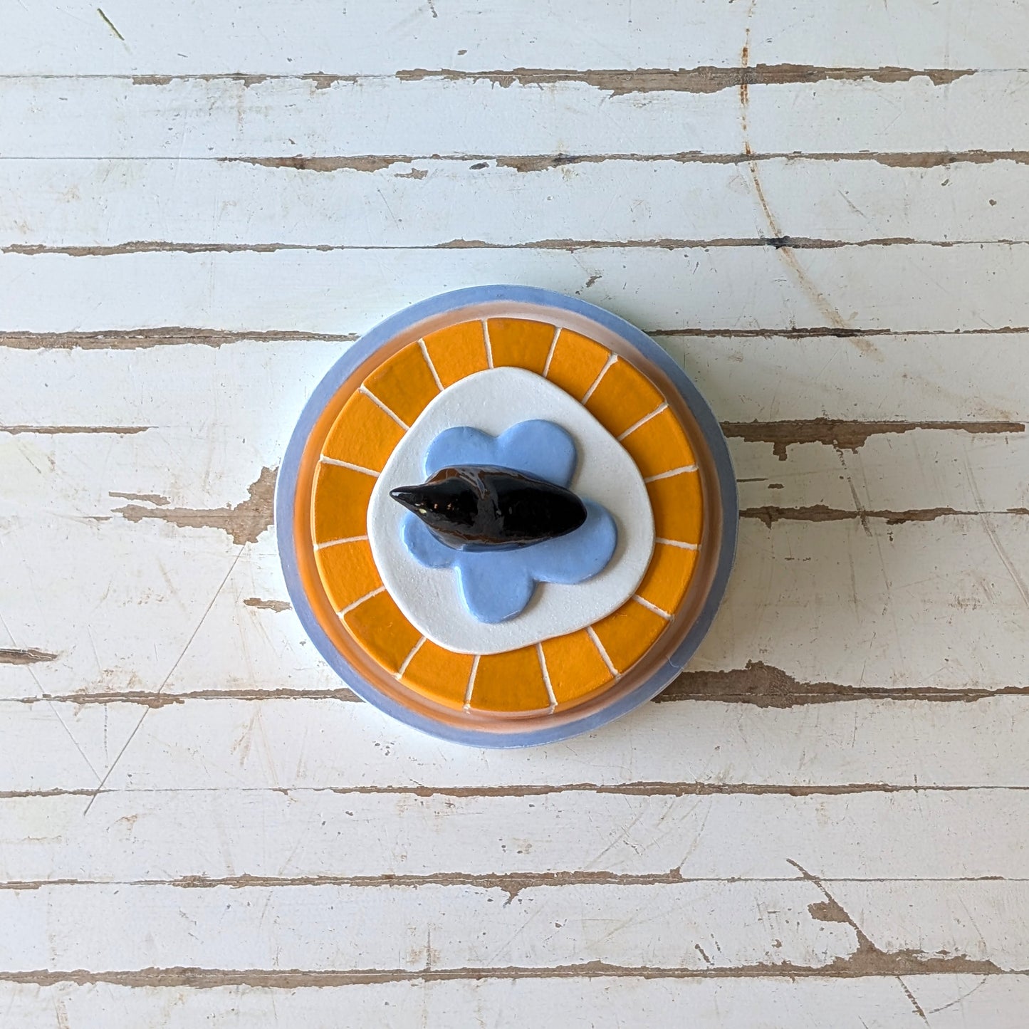 Top view of a colourful ceramic butter dish with a bird handle on a wooden surface.