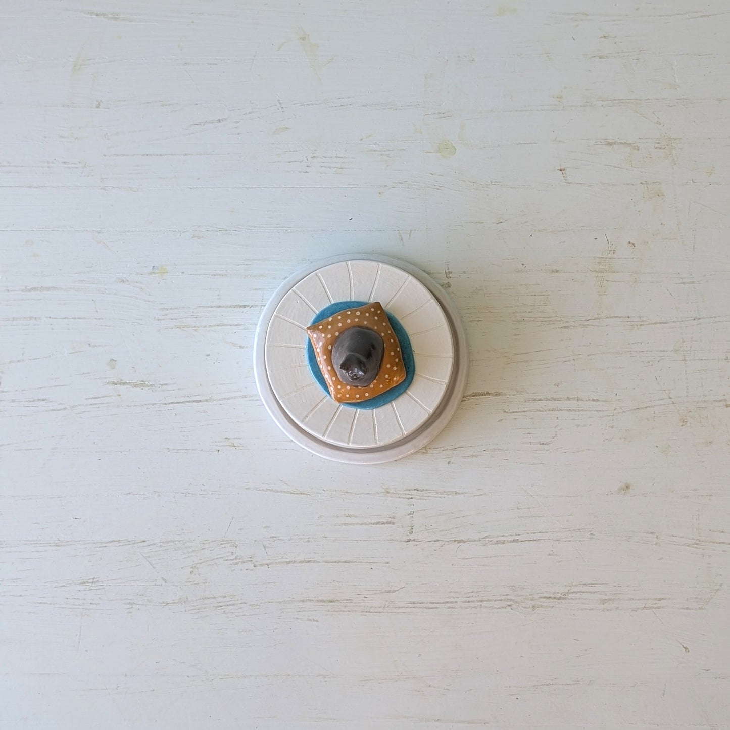 Round ceramic butter dish with decorative elements on a light wooden surface