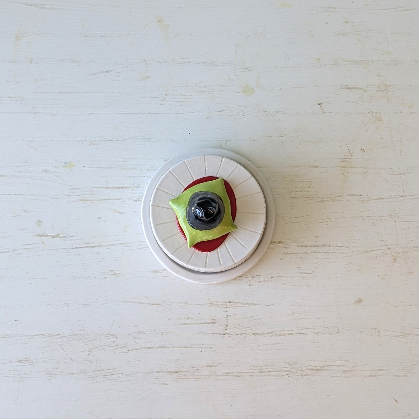 Round butter dish with white base, green top, and black center on a light wooden surface