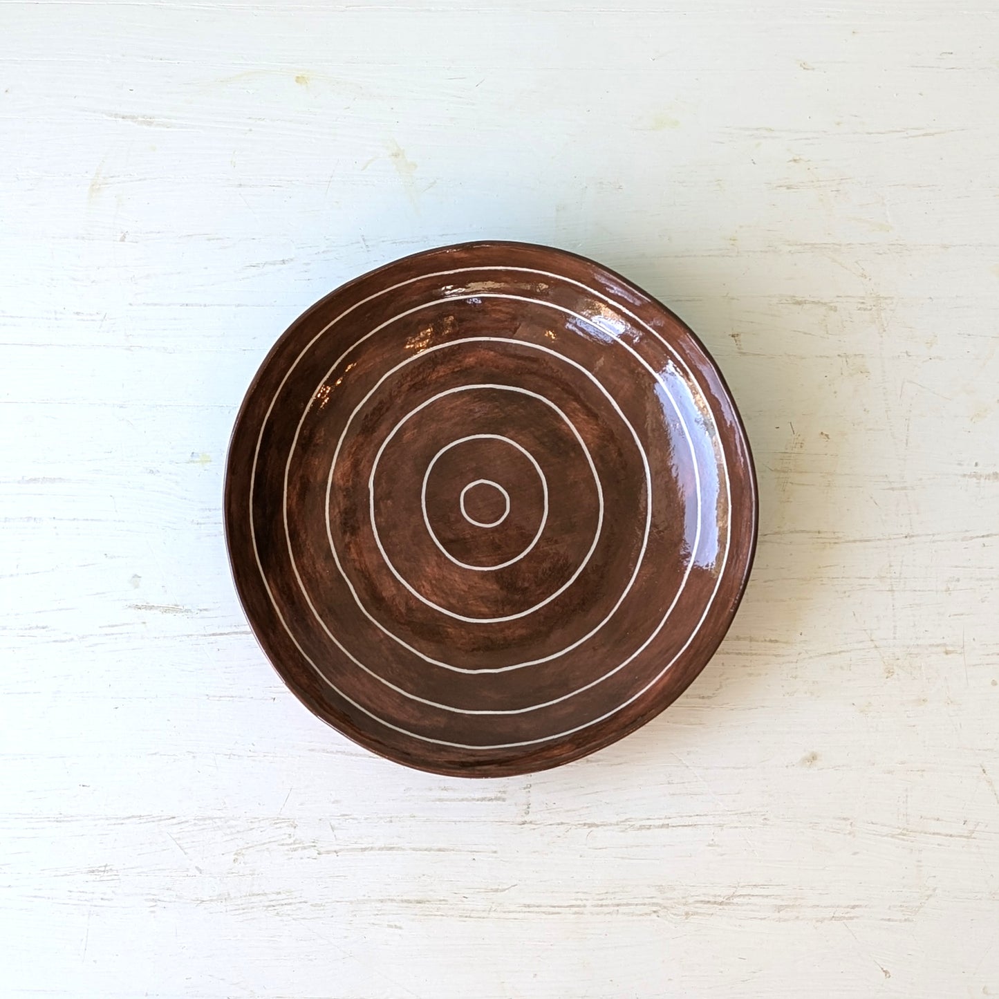 Brown ceramic plate with carved concentric circles on white table