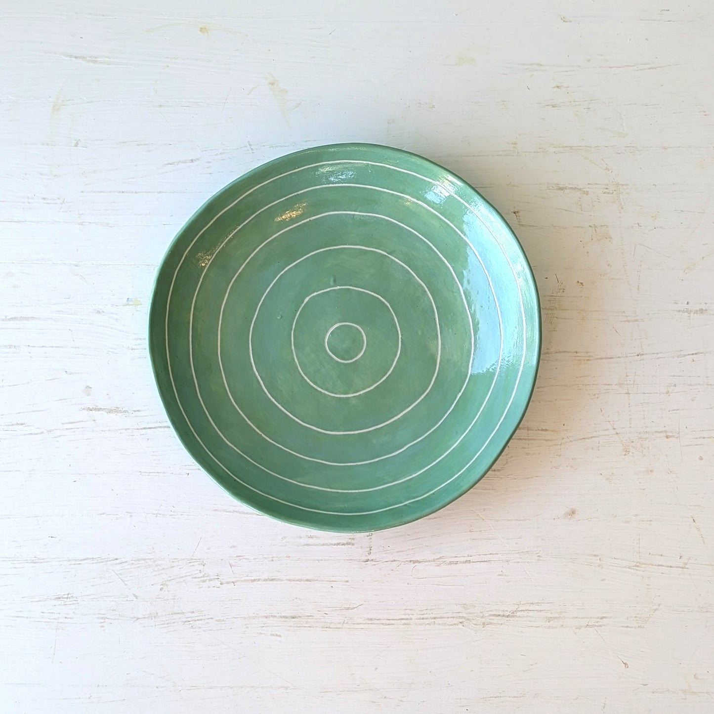 Green ceramic plate with carved concentric circles on a white table