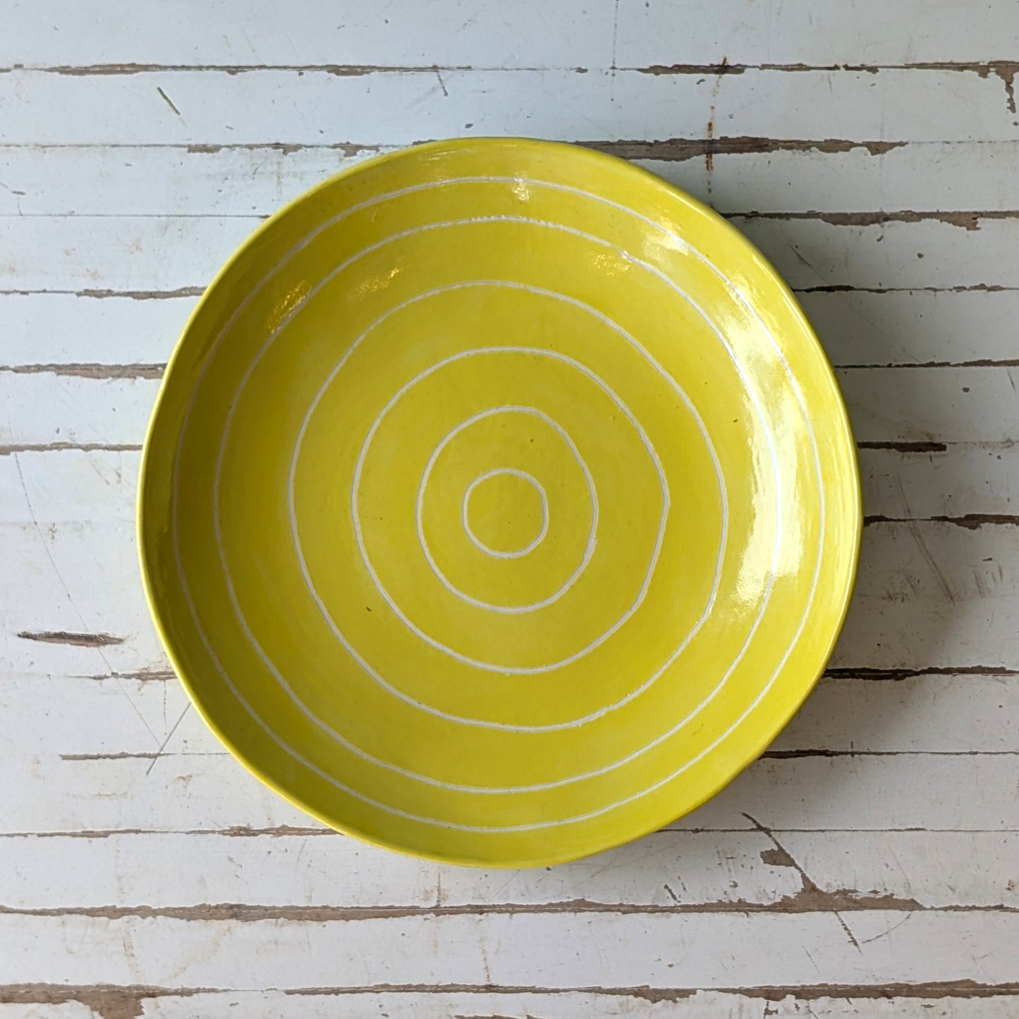 Top view of a yellow ceramic plate with carved concentric circles on a white wooden surface.