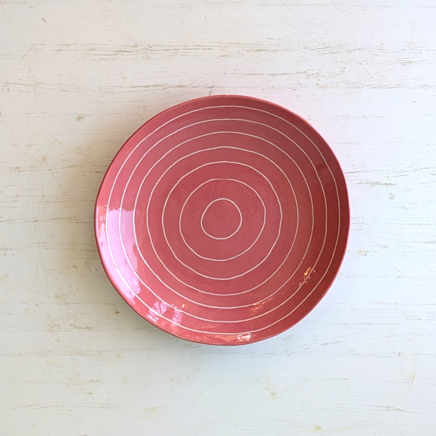 Pink ceramic plate with carved concentric circles on white table