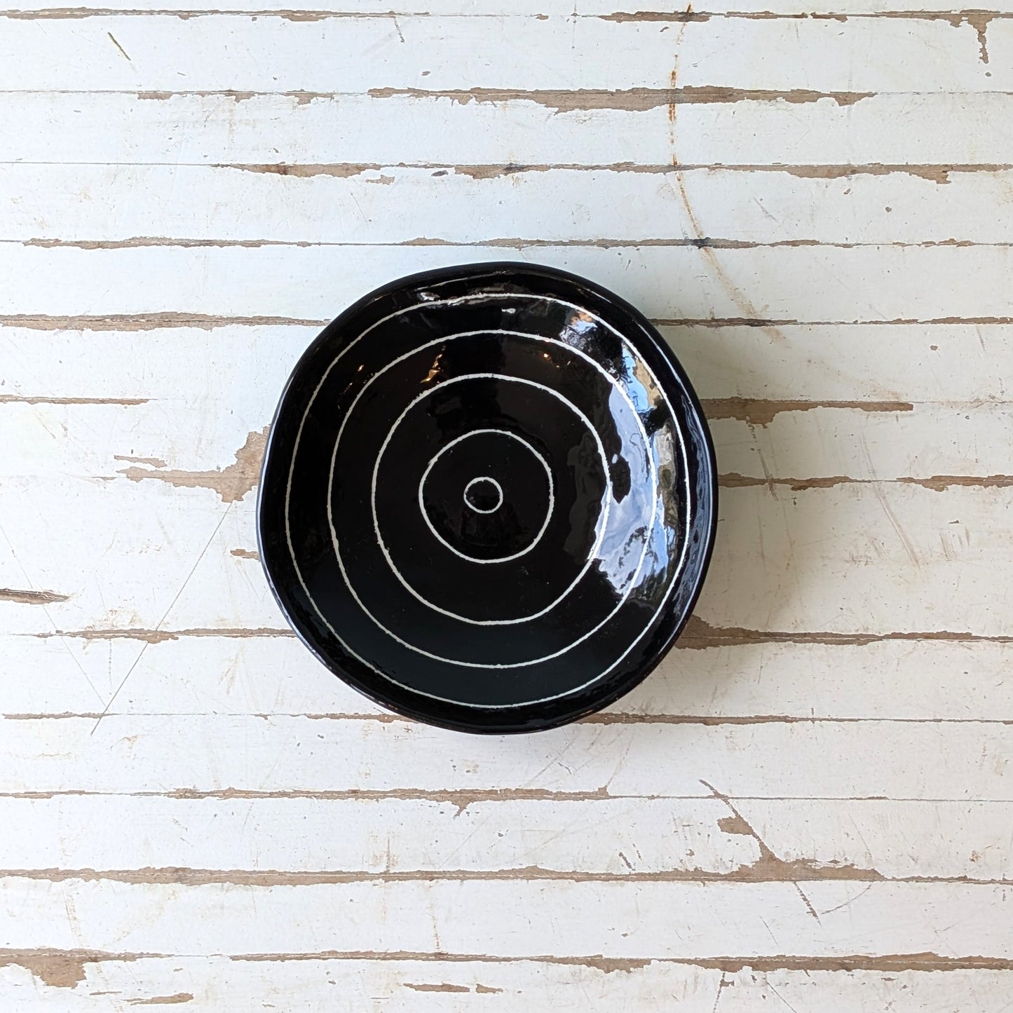 Top view of a black ceramic bowl with carved concentric circles on a white wooden surface.