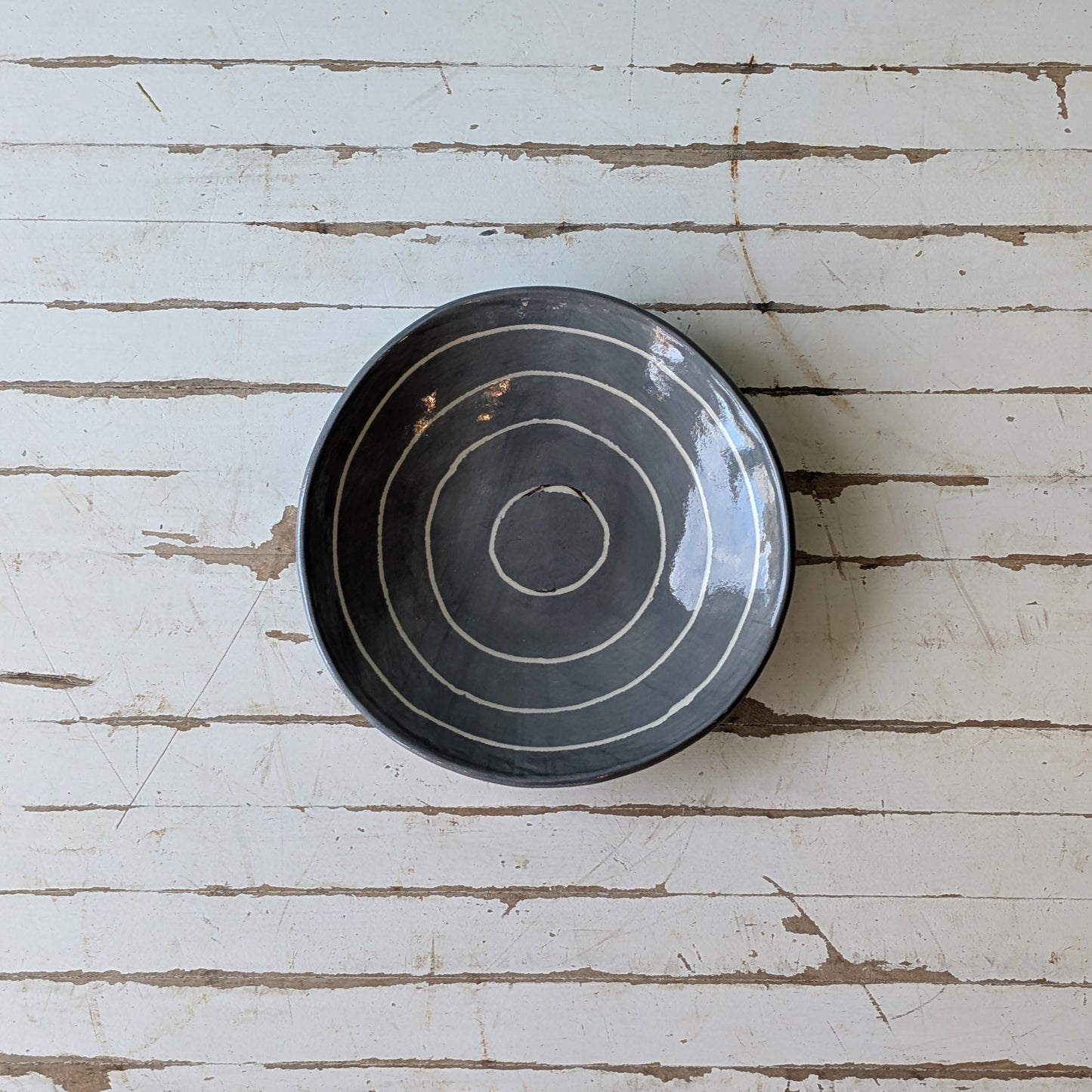 Top view of a grey ceramic bowl with carved concentric circles on a white wooden table.