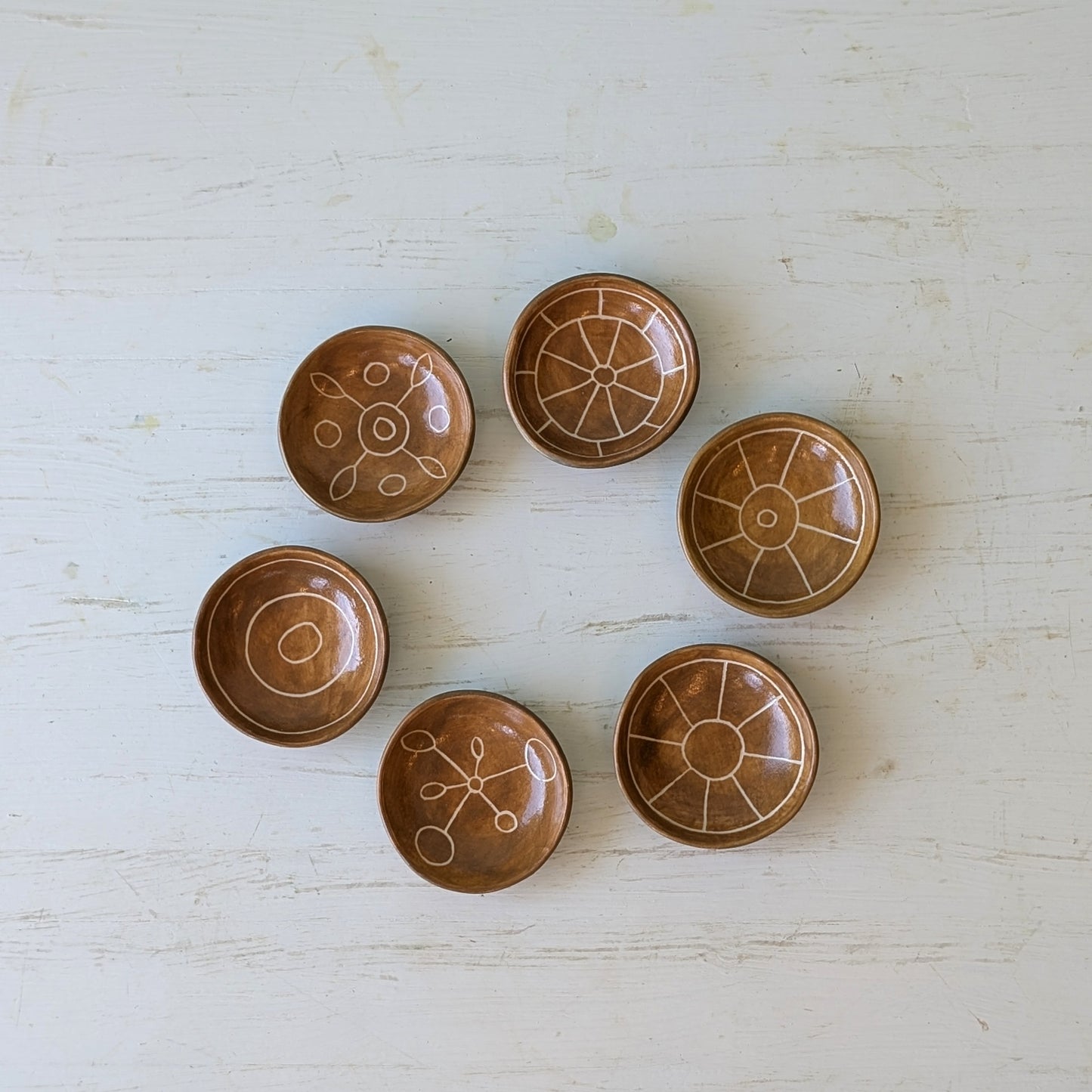Set of six brown ceramic bowls with decorative patterns on a light wooden surface