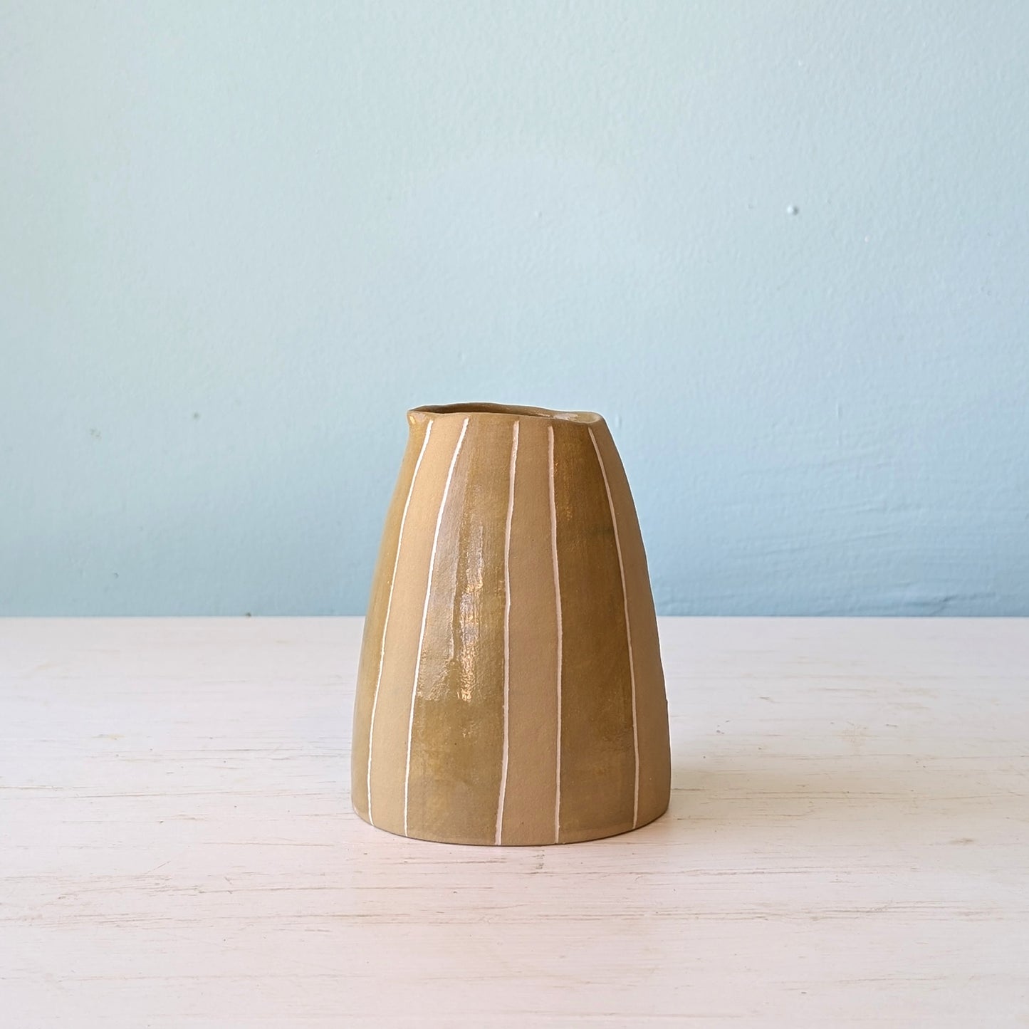 Brown ceramic jug on white table against blue wall