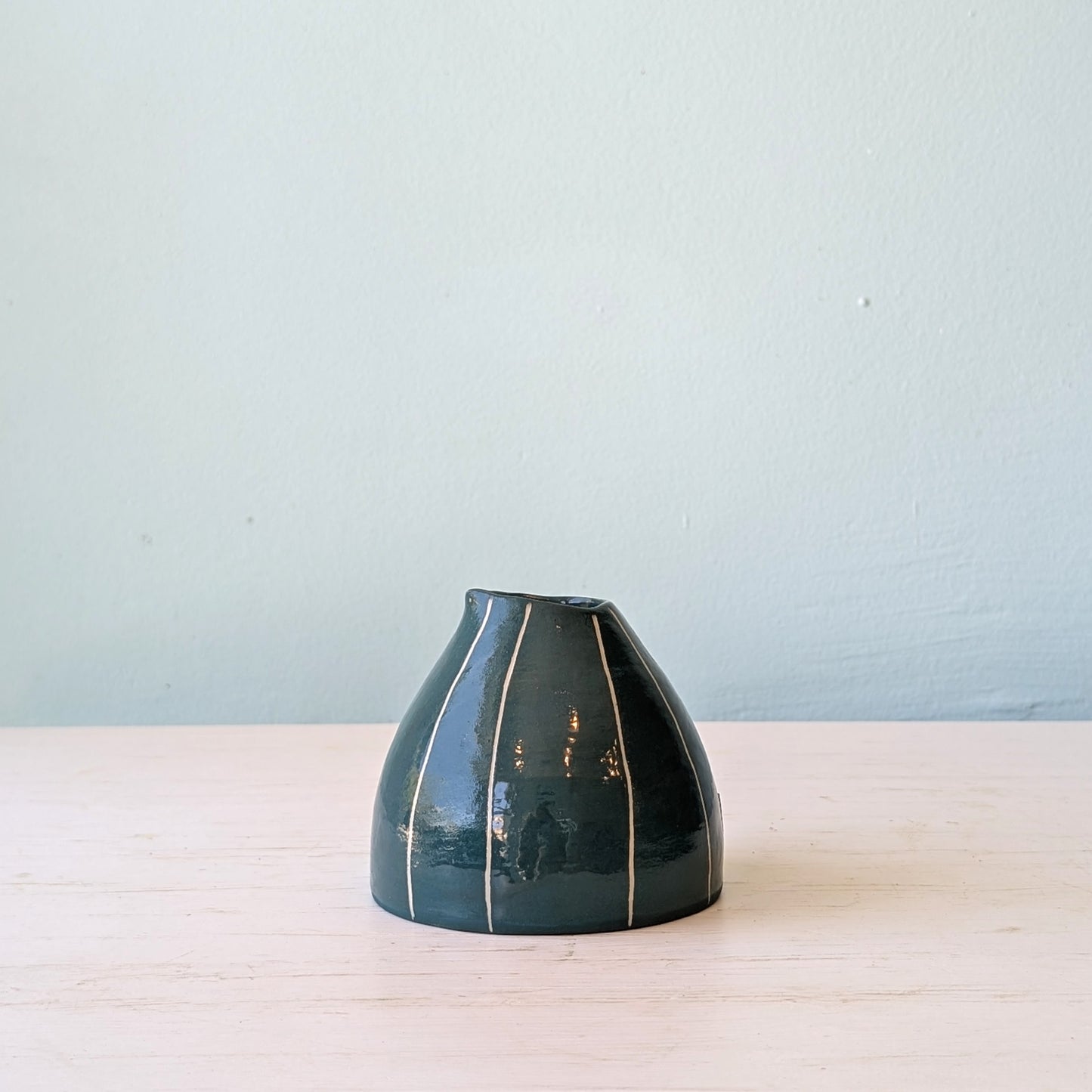 Dark green ceramic jug on white table against blue wall