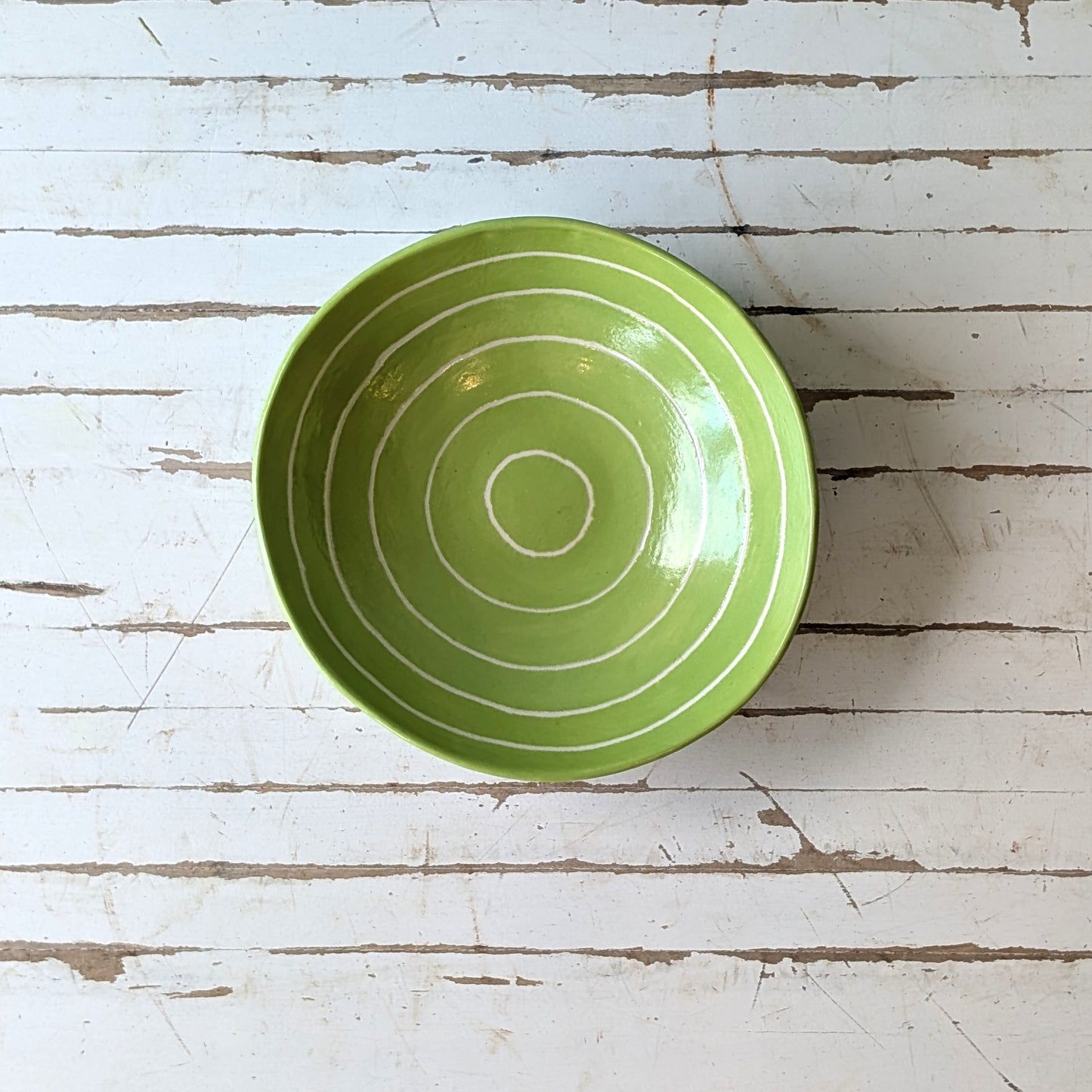 Top view of a green ceramic bowl with carved concentric circles on a white wooden surface.