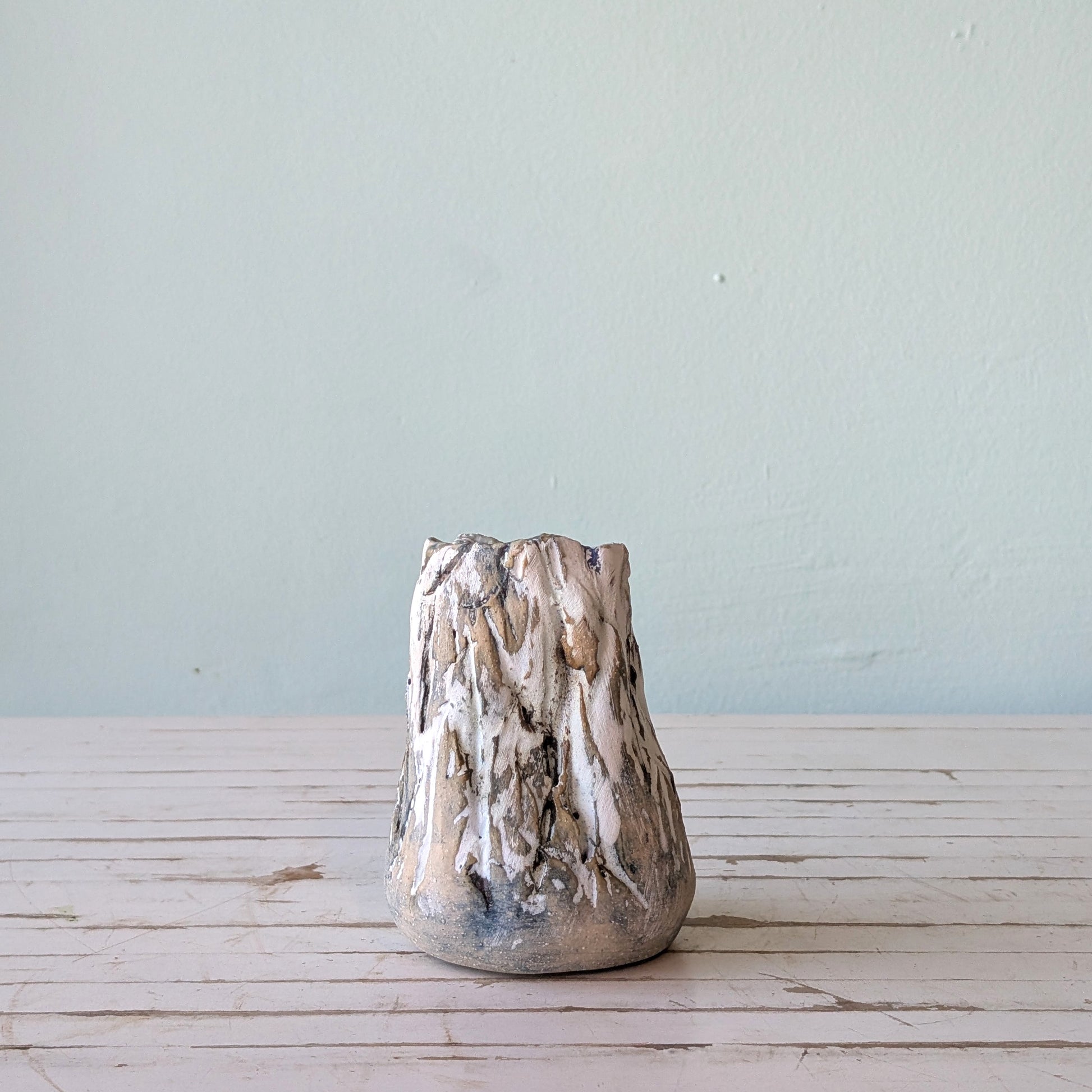 Front view of a beige stoneware vase with thick black and white glaze and vertical scoring, resembling the surface of tree bark.