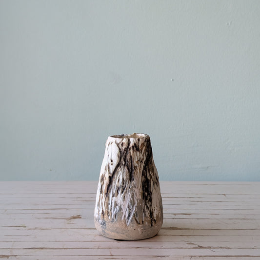 Front view of a beige stoneware vase with thick black and white glaze and vertical scoring, resembling the surface of tree bark.